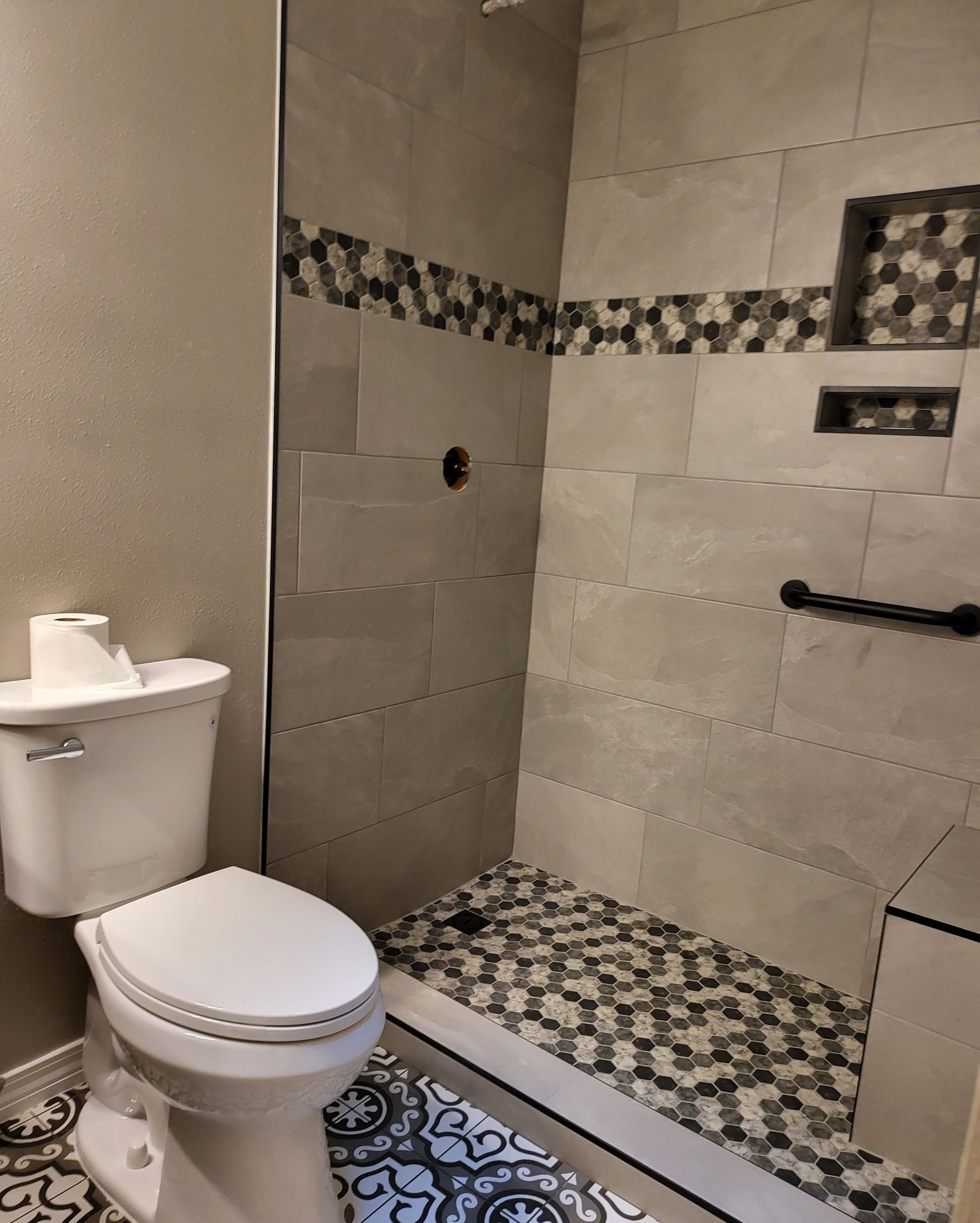 Small bathroom with toilet, pedestal sink, and tiled walk-in shower with grab bar and mosaic floor.