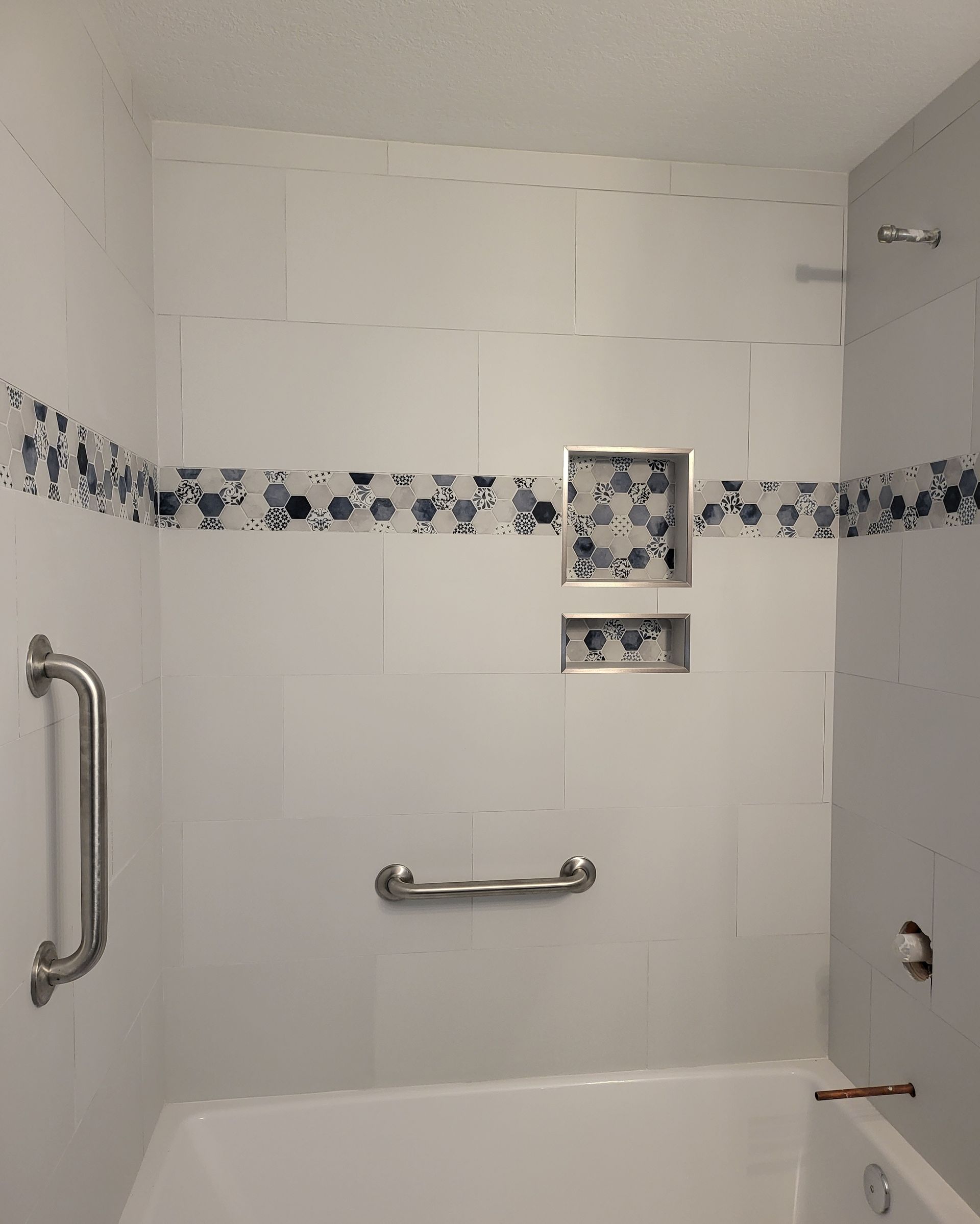 White-tiled bathroom shower with grab bars and blue floral accent strip on the wall.