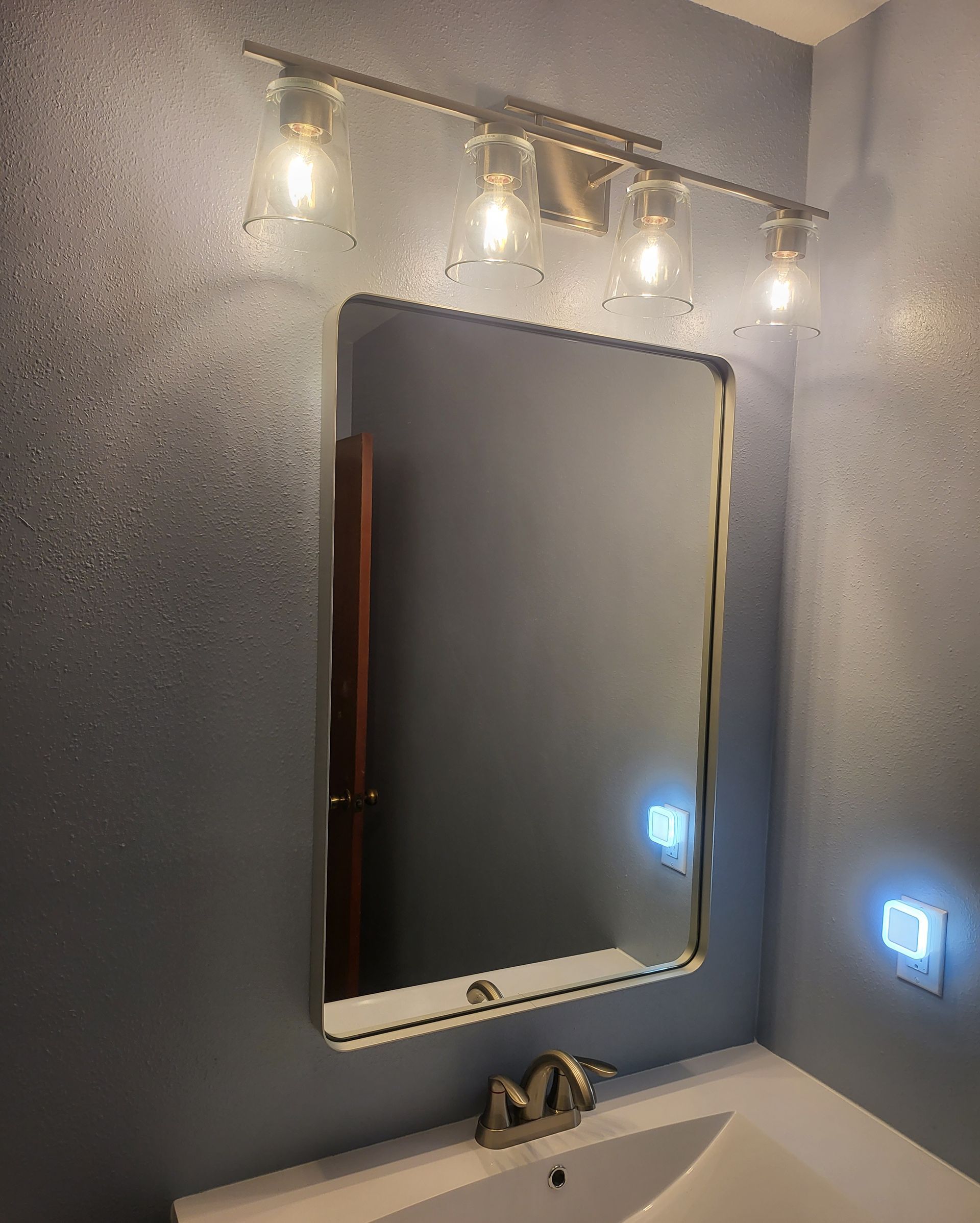 Bathroom vanity with gray walls, lit mirror, wall sconces, and sink below
