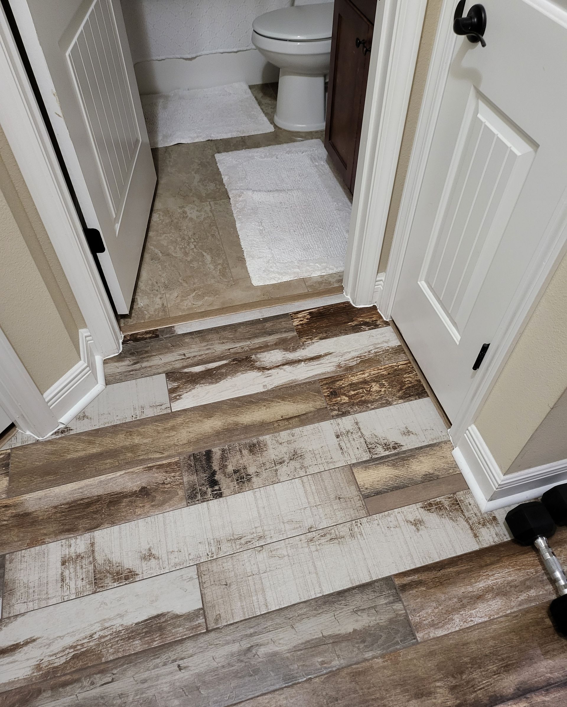 Damaged, worn floorboards at a bathroom doorway with peeling white finish and exposed wood