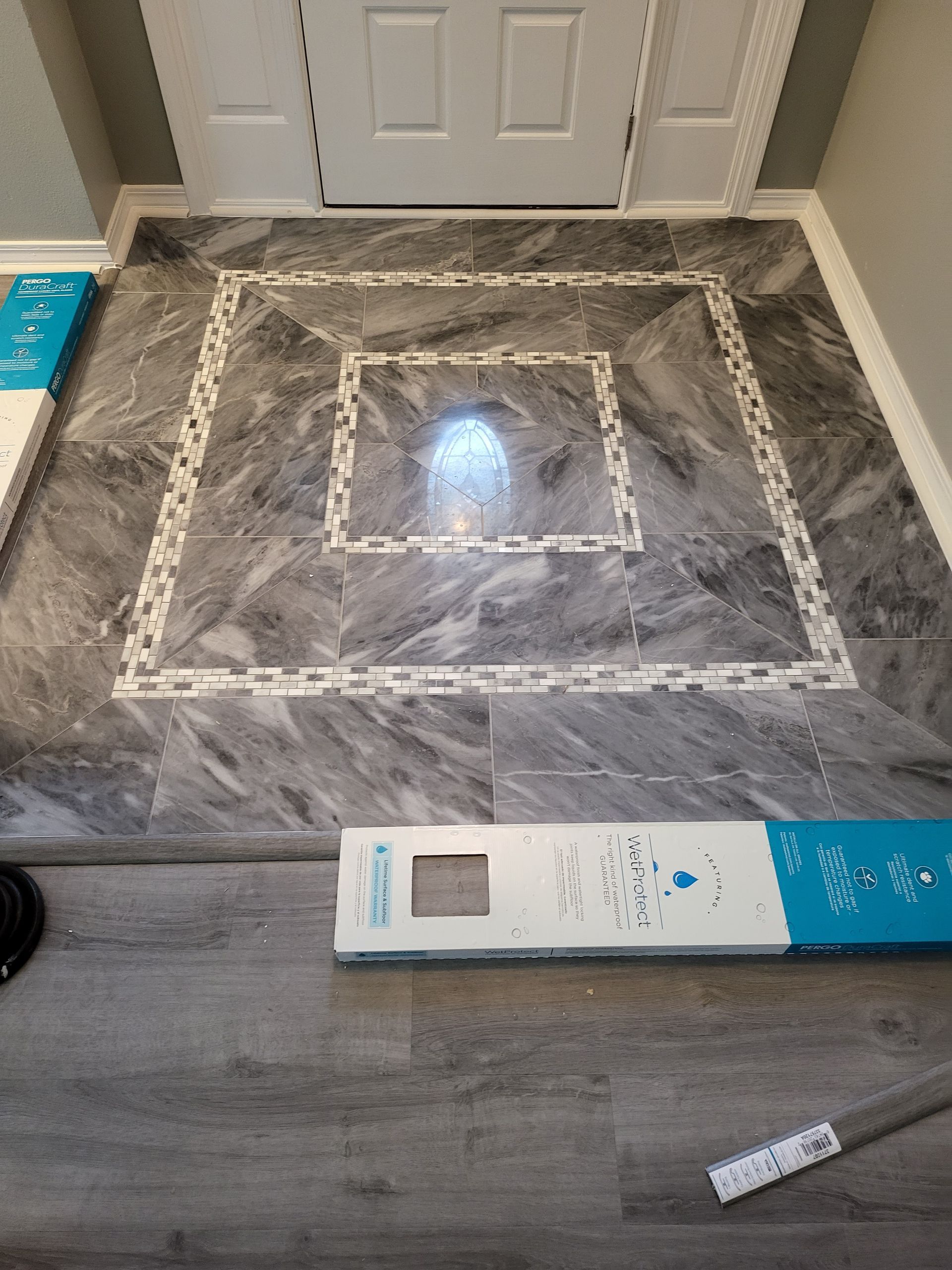 Marble-look floor tile layout with taped square in front of a white door, with boxes on the floor.