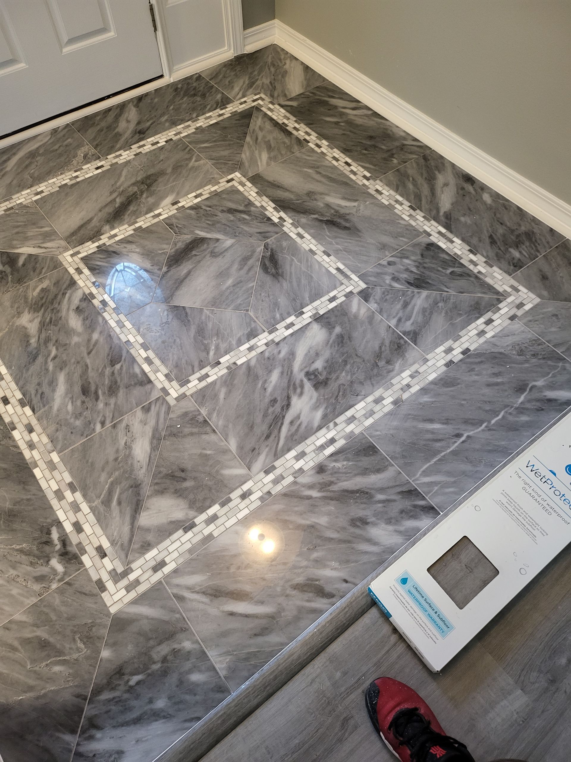 Gray marble-tile floor with decorative white border inlay and a cardboard box at the edge