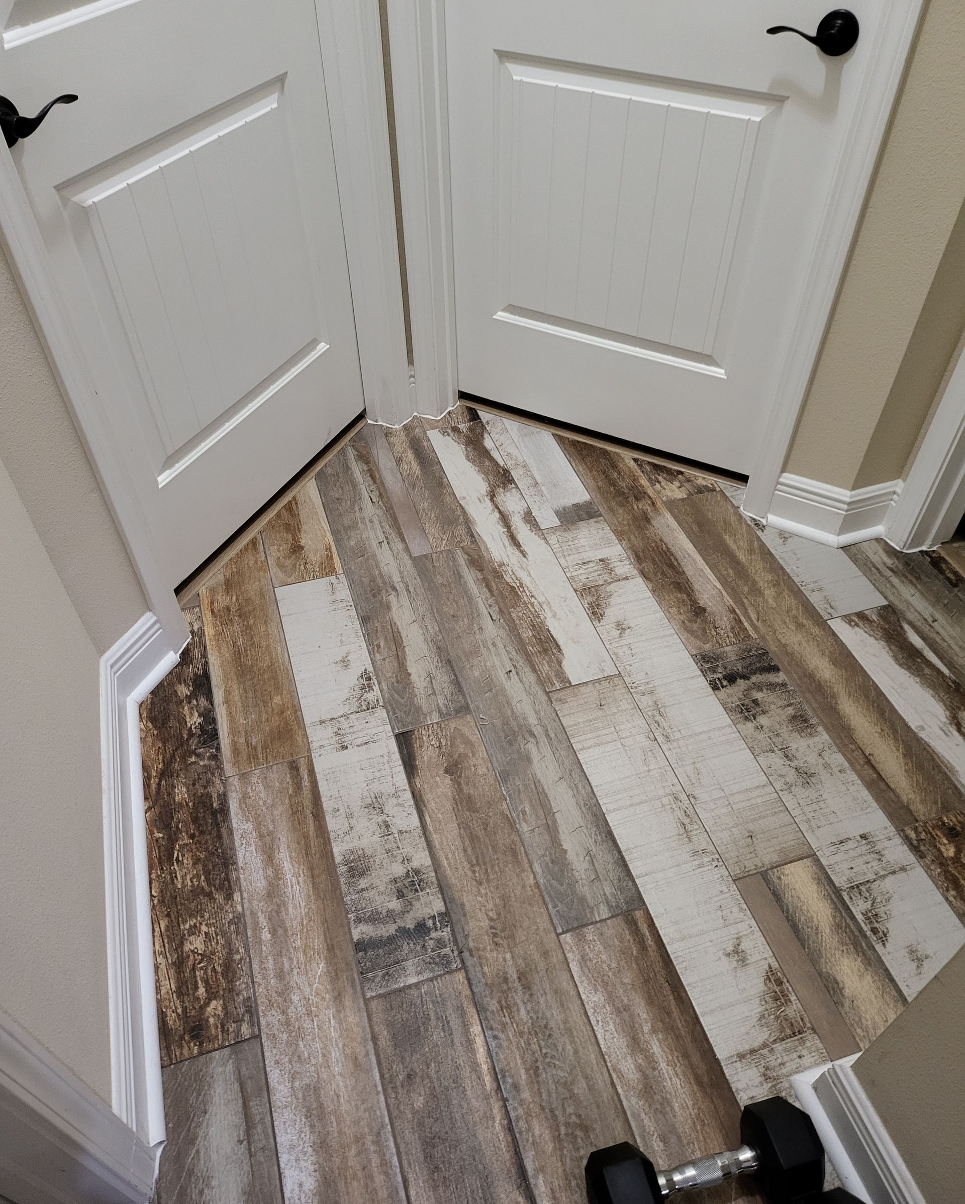 Hallway with closed white double doors and weathered wood-look flooring in beige and gray tones