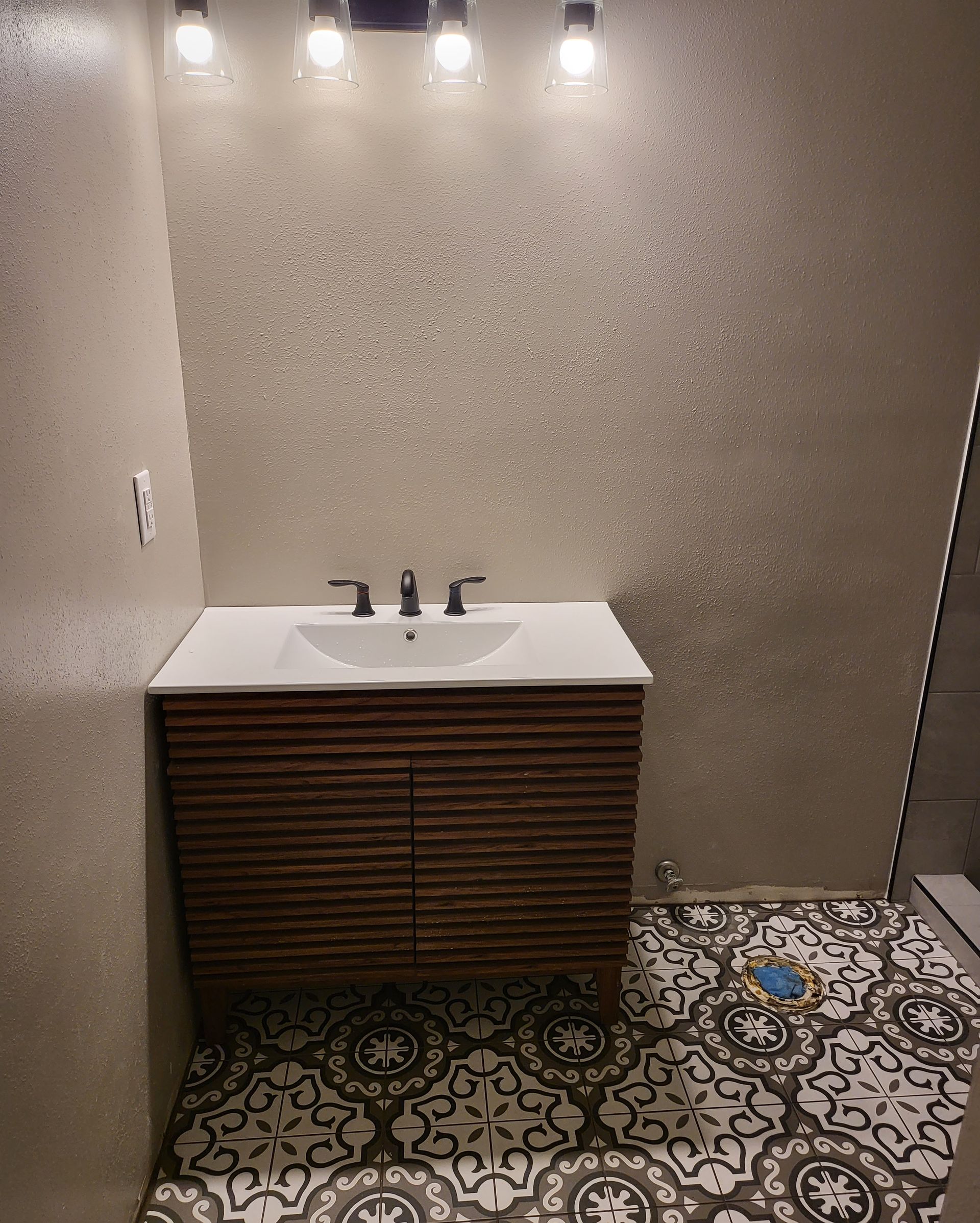 Small bathroom with patterned tile floor, floating sink vanity, and three lights above the mirror.
