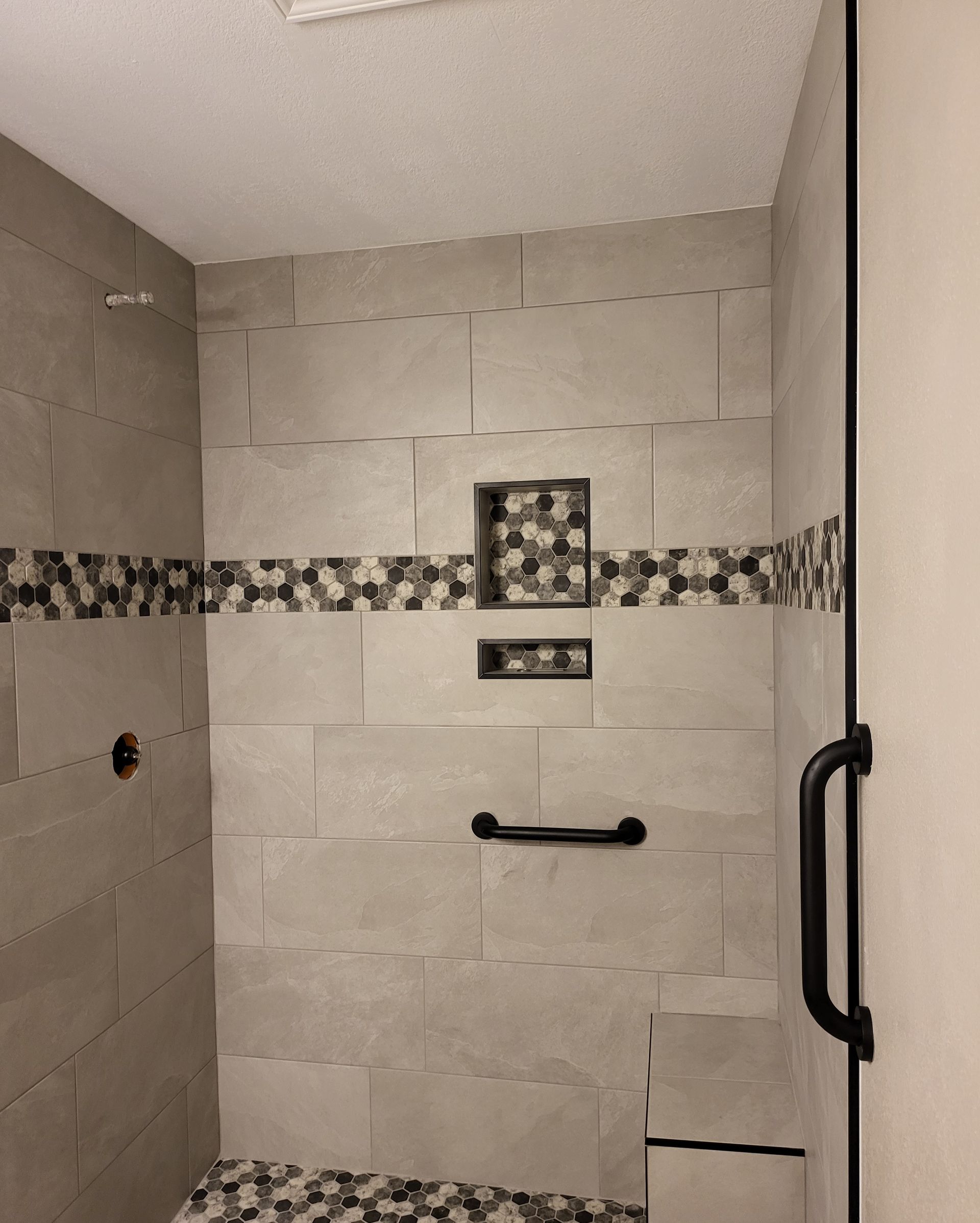Tiled walk-in shower with gray walls, decorative accent strip, grab bar, and a shower valve opening.