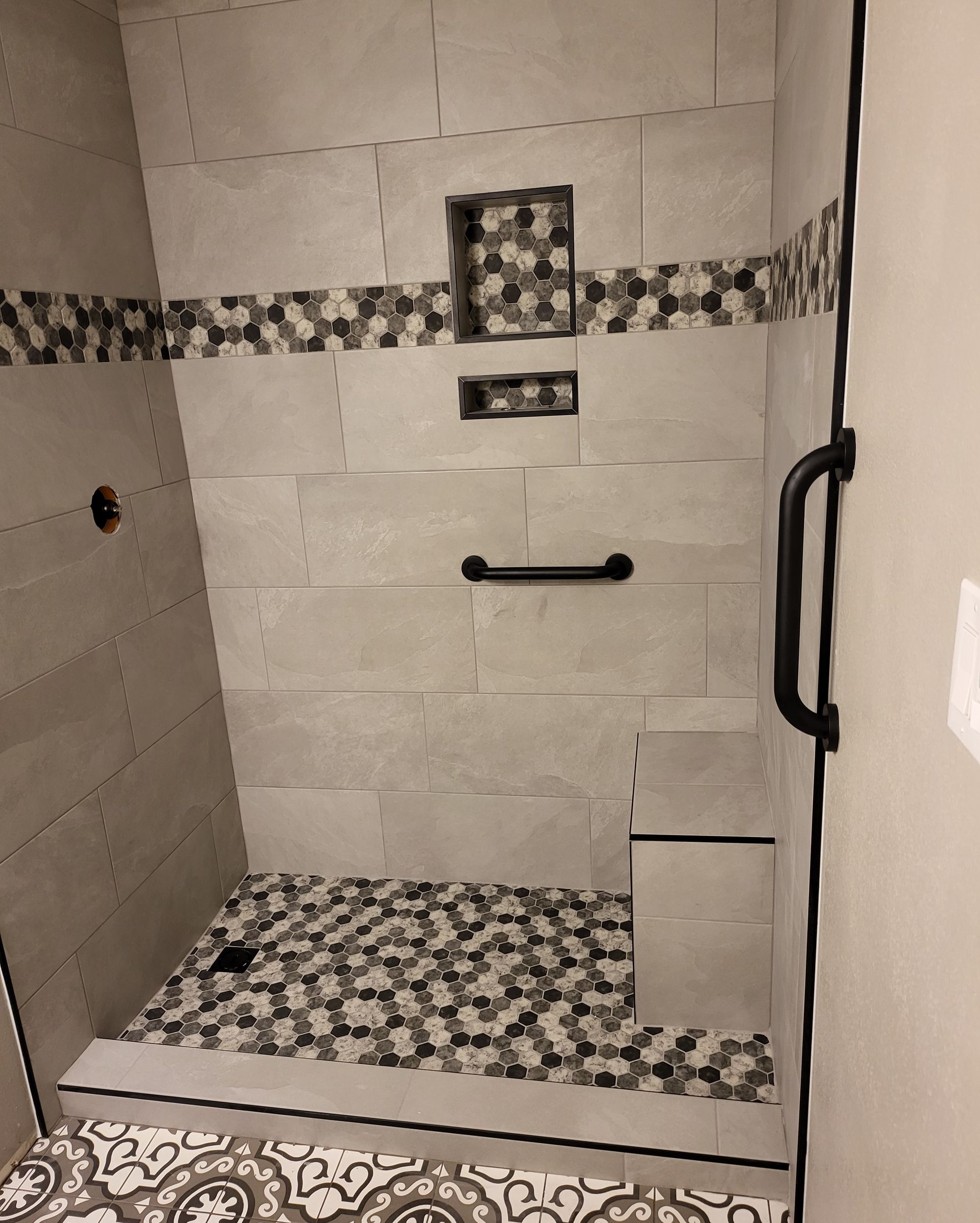 Tiled walk-in shower with mosaic trim, handheld shower fixture, grab bar, and bench seat