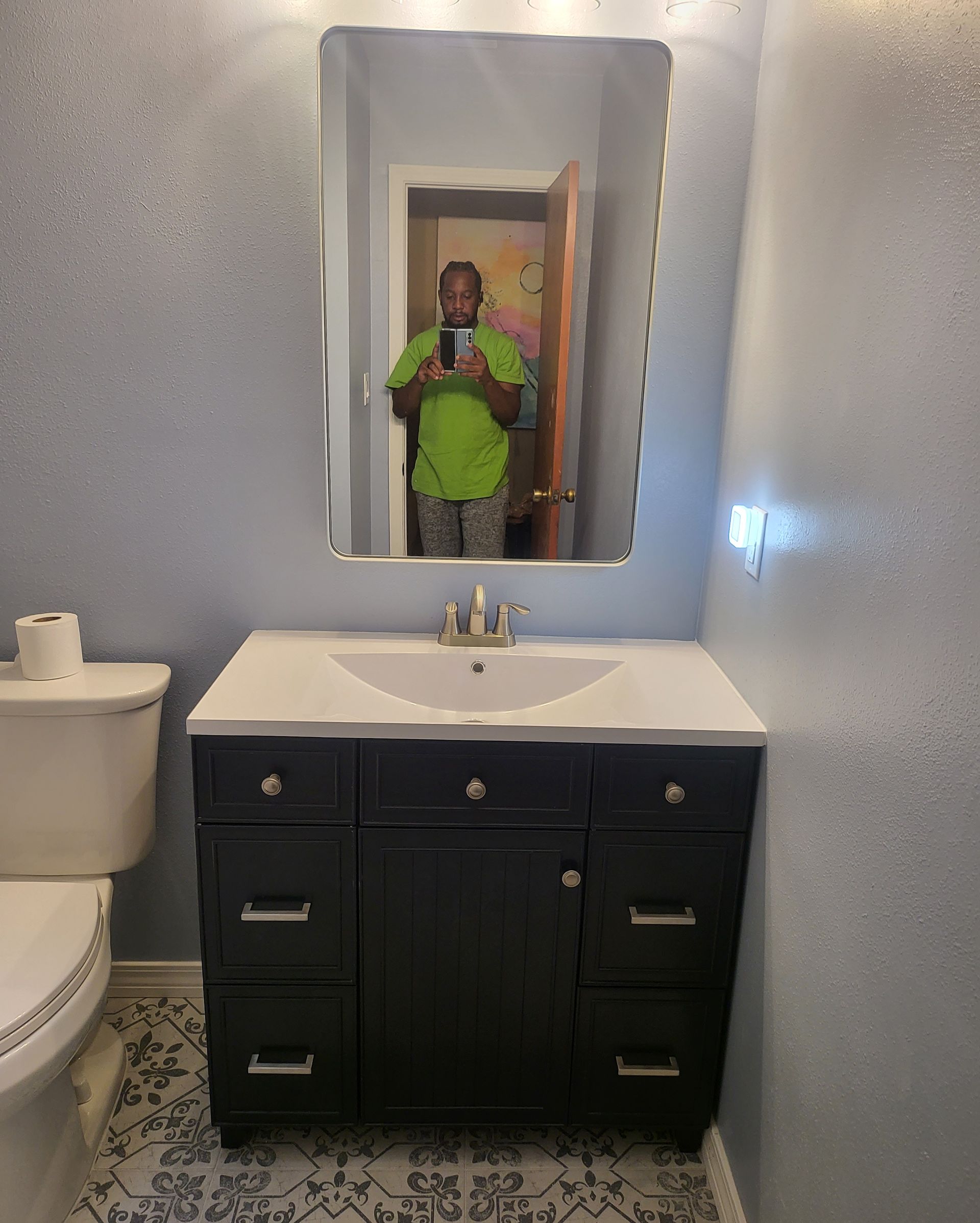 Bathroom with dark vanity, white sink, mirror, and a person taking a mirror selfie.
