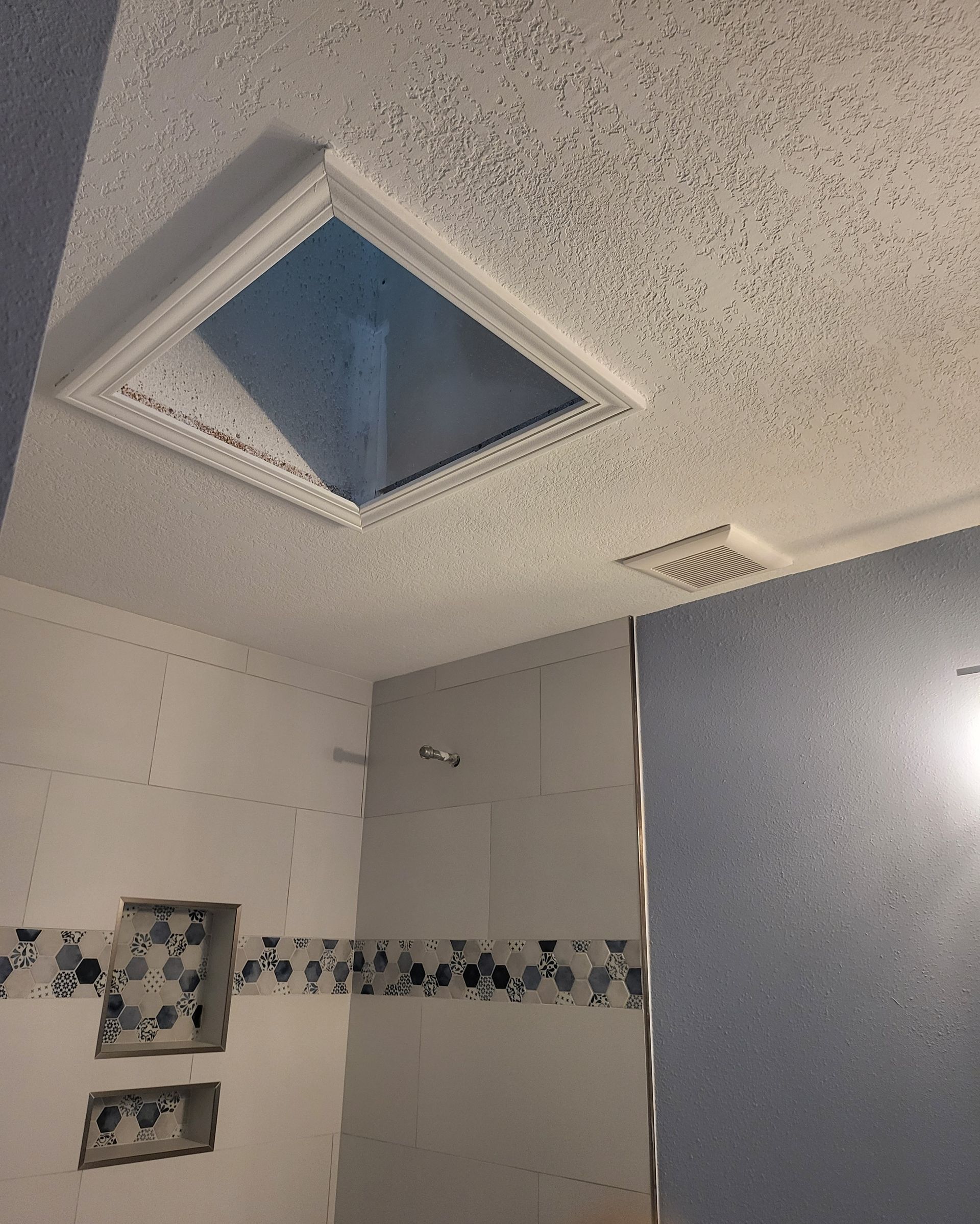Bathroom ceiling with a skylight, white textured tiles, and a wall mirror below.
