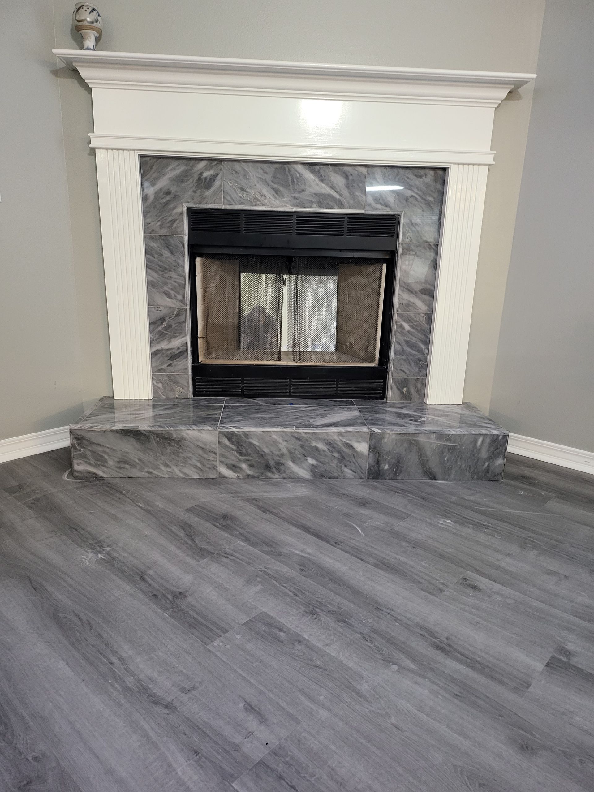Empty room with a gray wood floor and a white fireplace with black insert and gray tile hearth.