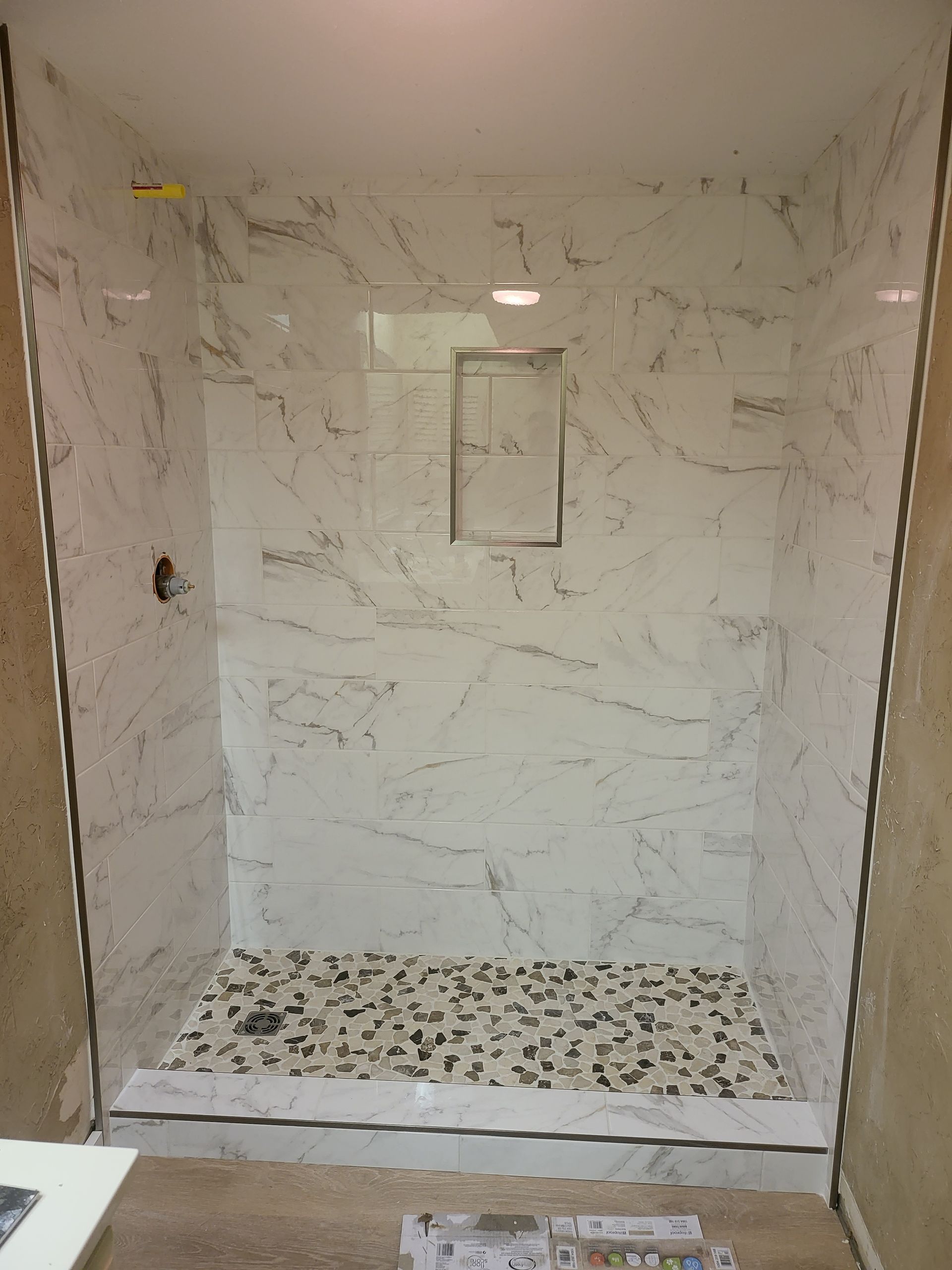 Empty tiled shower stall with a patterned pebble floor and recessed shelf in the back wall