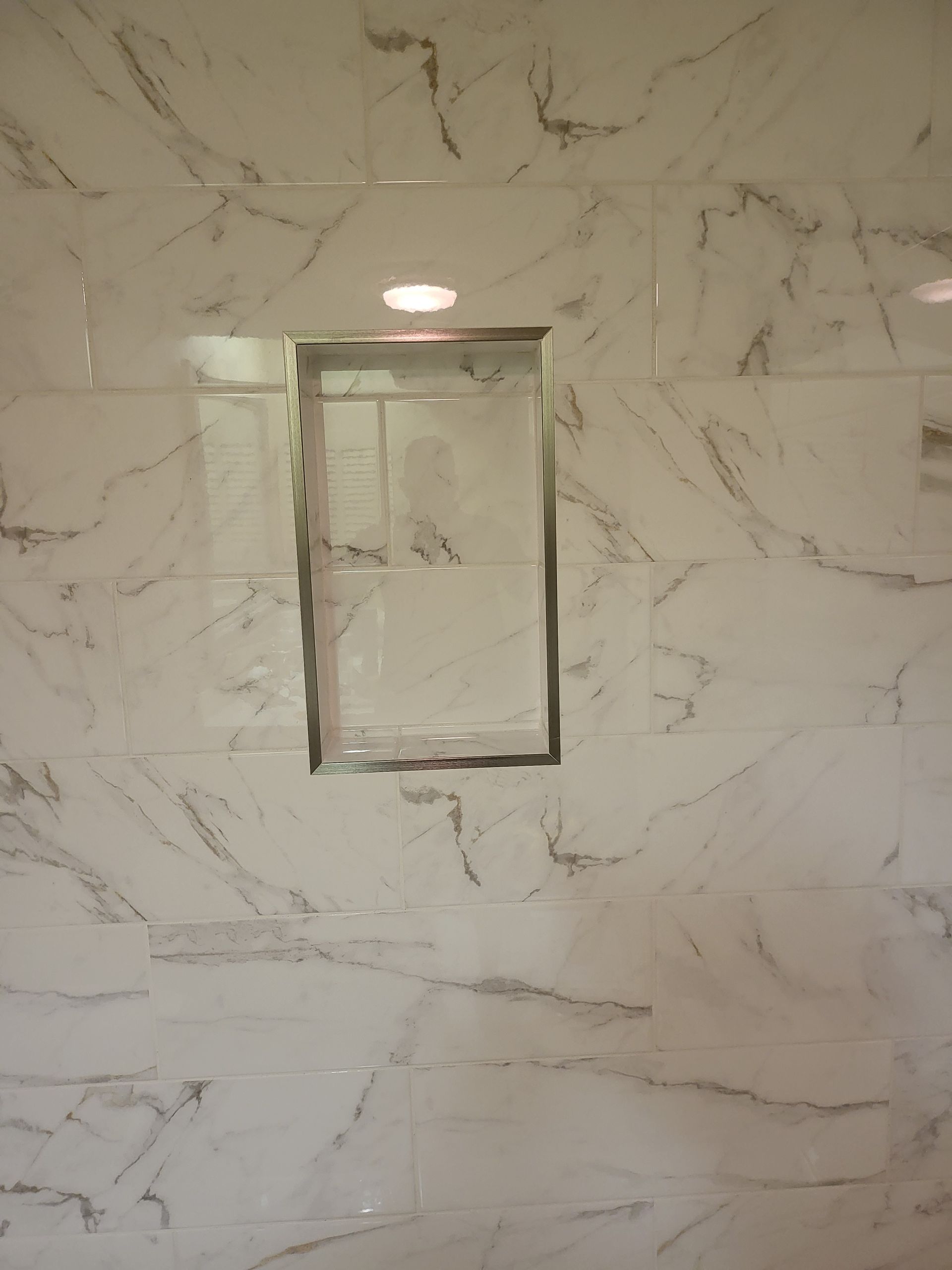 Marble-tiled wall with a small recessed rectangular cabinet or niche centered beneath a light.