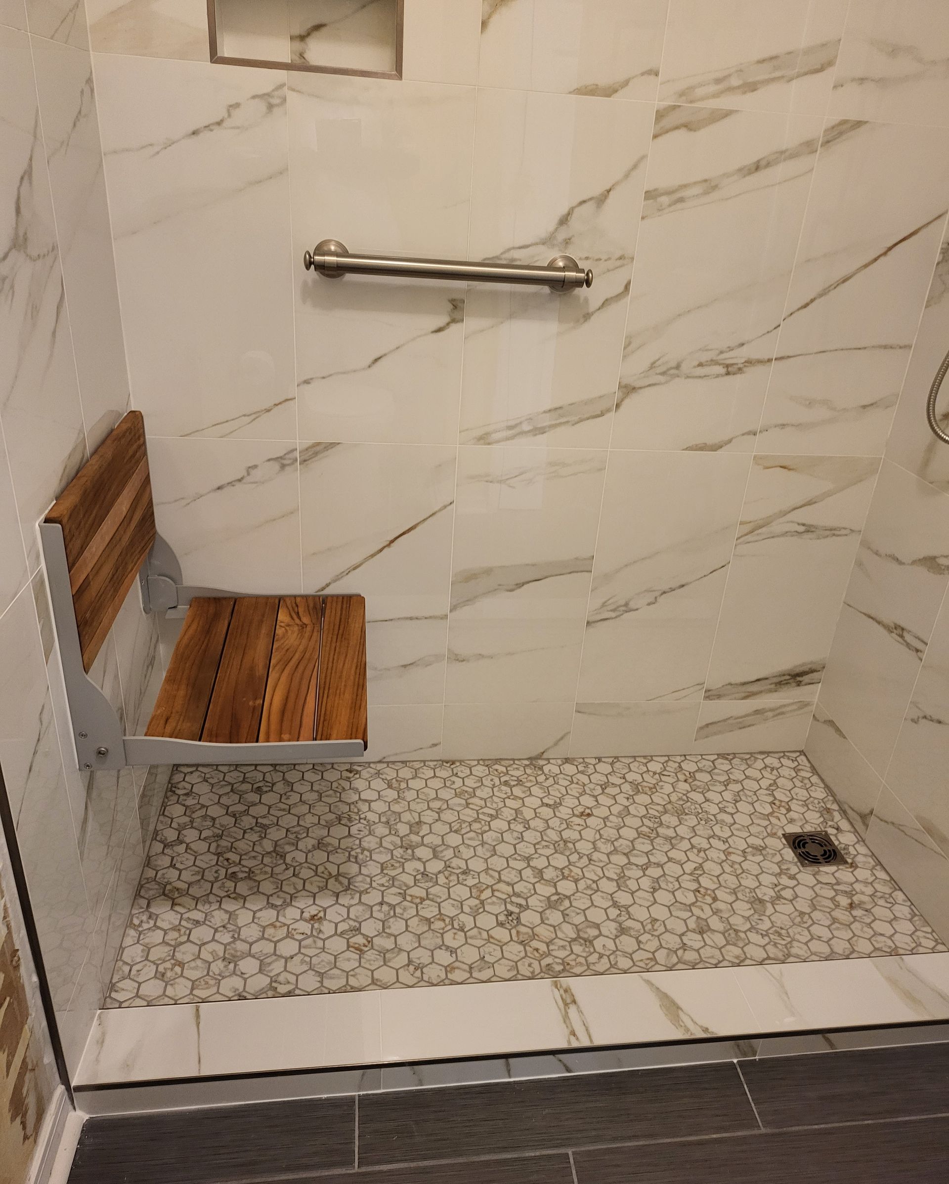Accessible shower with bench, grab bar, and handheld showerhead on marble-pattern tile.