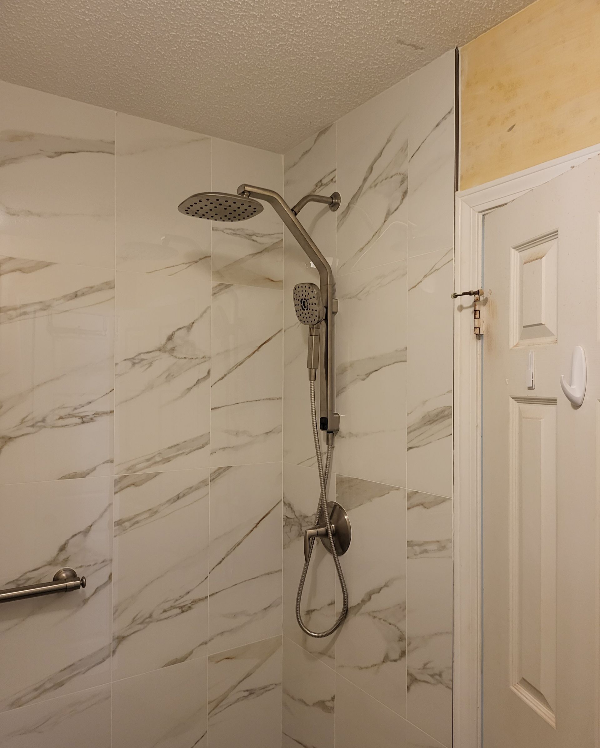 Bathroom shower with marble-pattern tile, a handheld showerhead, and a shower door partially visible