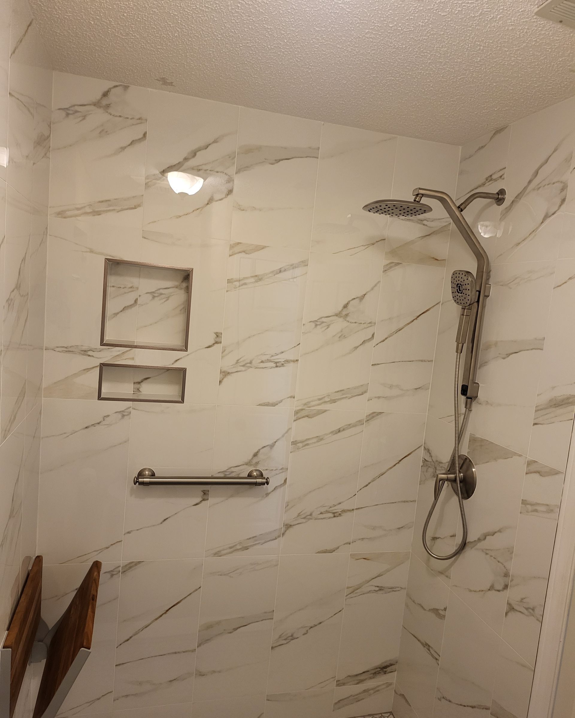 Modern tiled shower with rain head, handheld sprayer, niche shelves, and grab bar