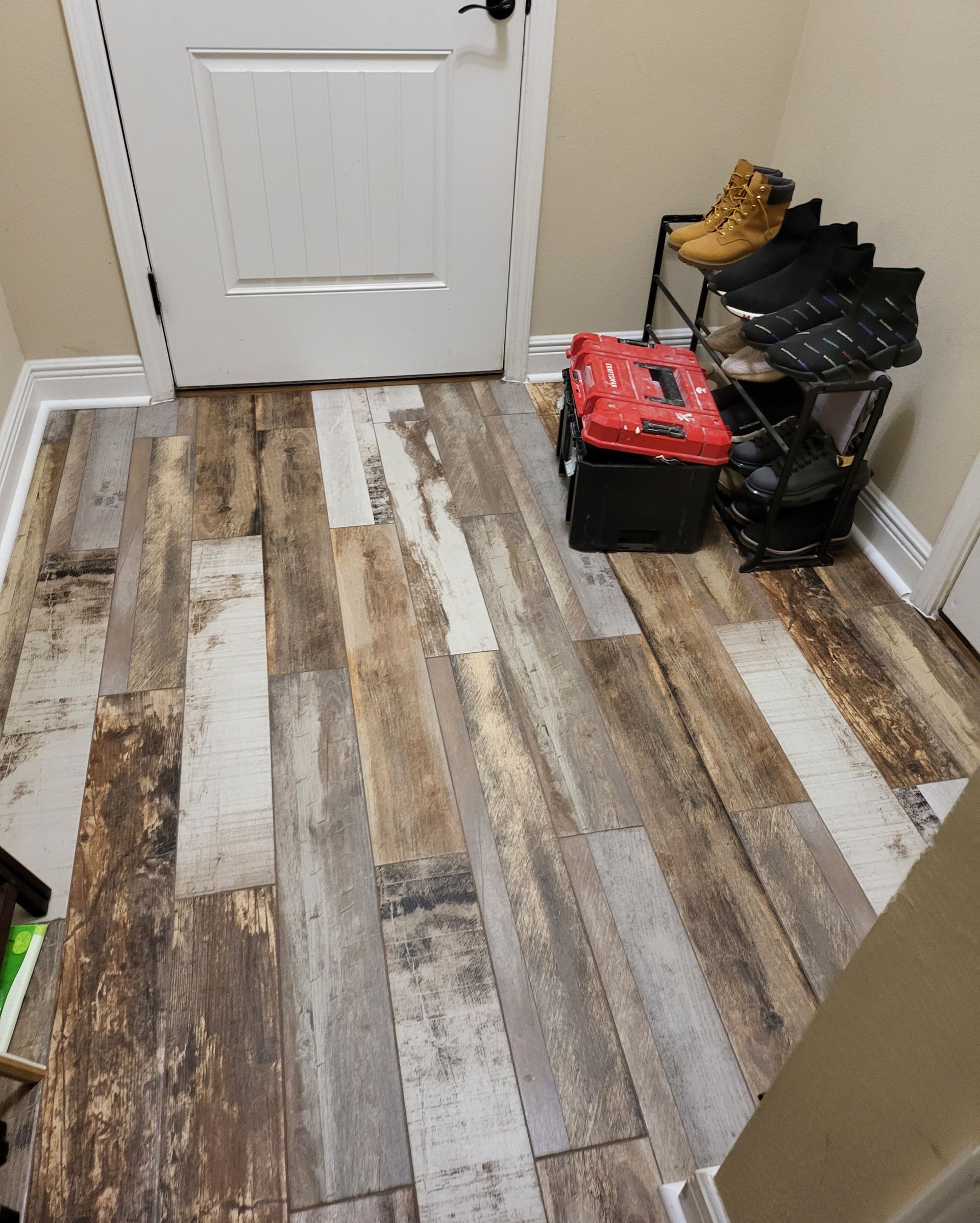 Hallway with wood-look tile floor, white door, and boots and storage bins stacked by the wall