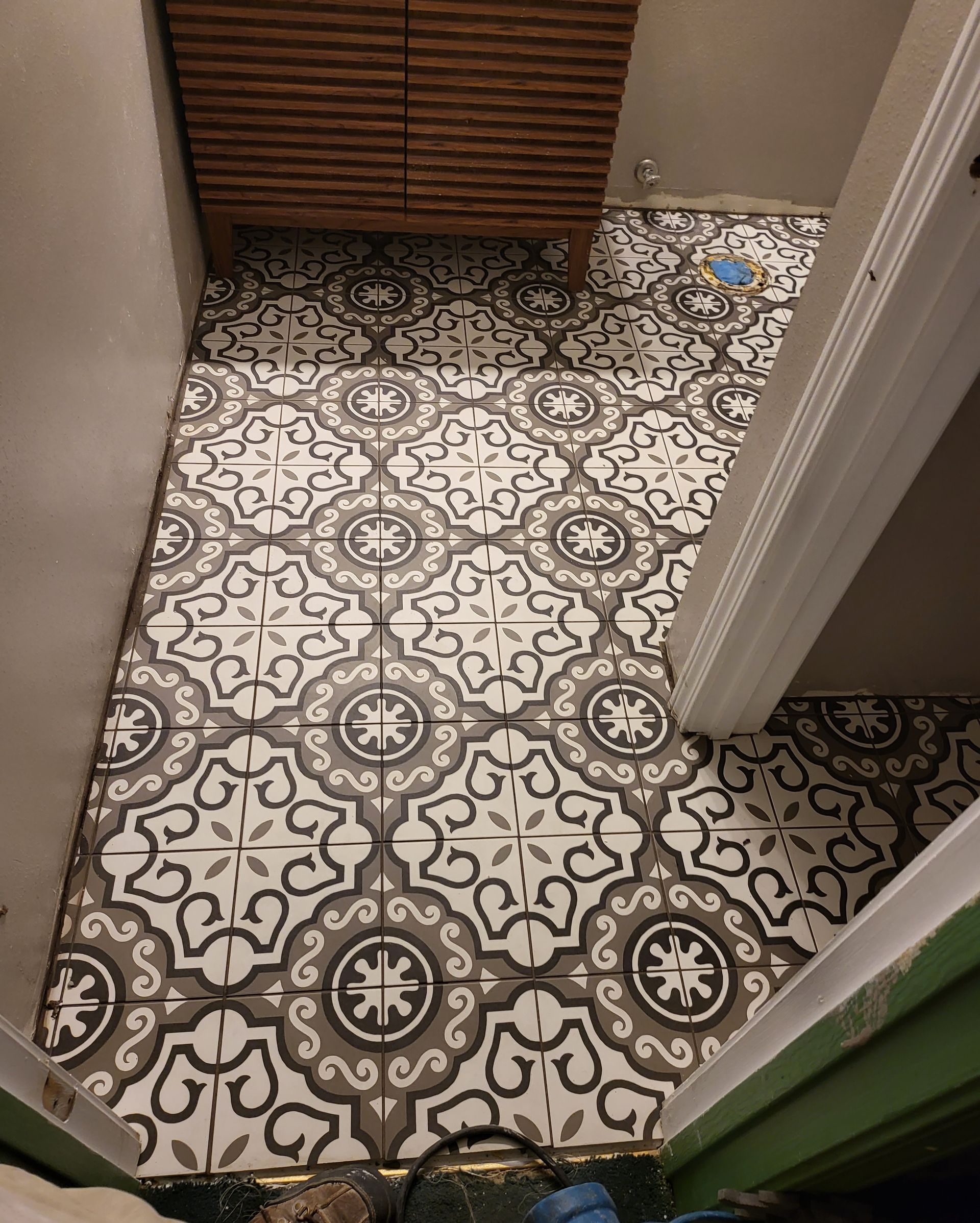 Small tiled hallway floor with patterned black-and-white tiles, a wooden cabinet, and a doorway with some clutter.