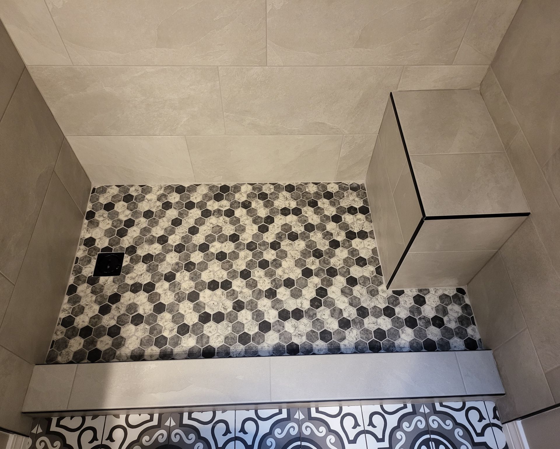 Small tiled shower with a mosaic floor, wall tiles, and a built-in bench.