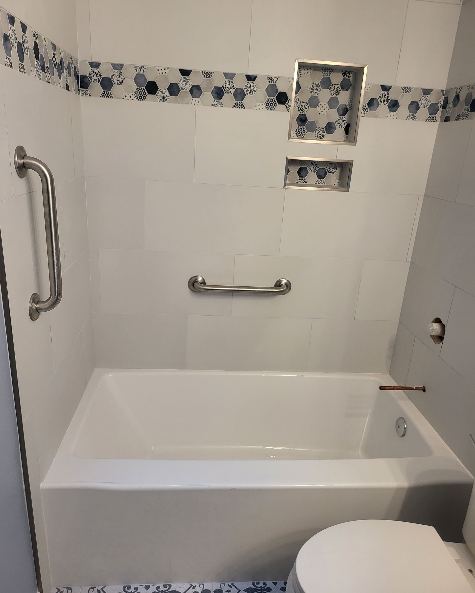 White tiled accessible bathtub with grab bars and blue decorative border, seen from above toilet.
