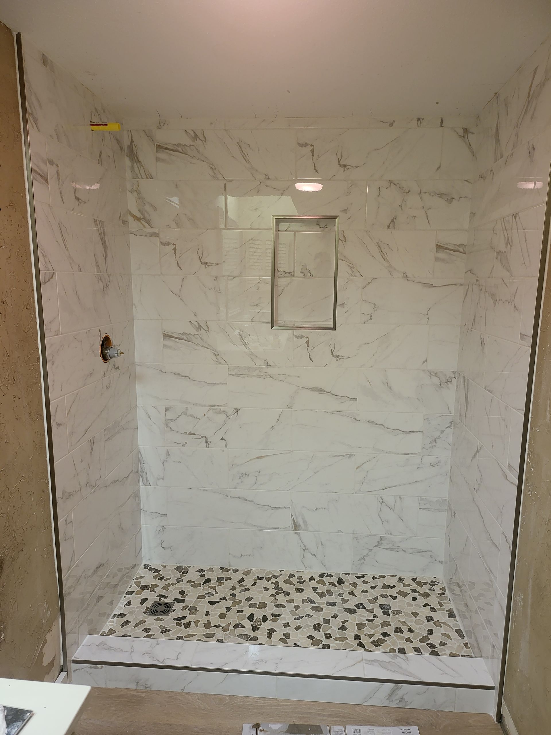 Empty tiled shower stall with marble-look walls, mosaic floor, and a recessed shelf.