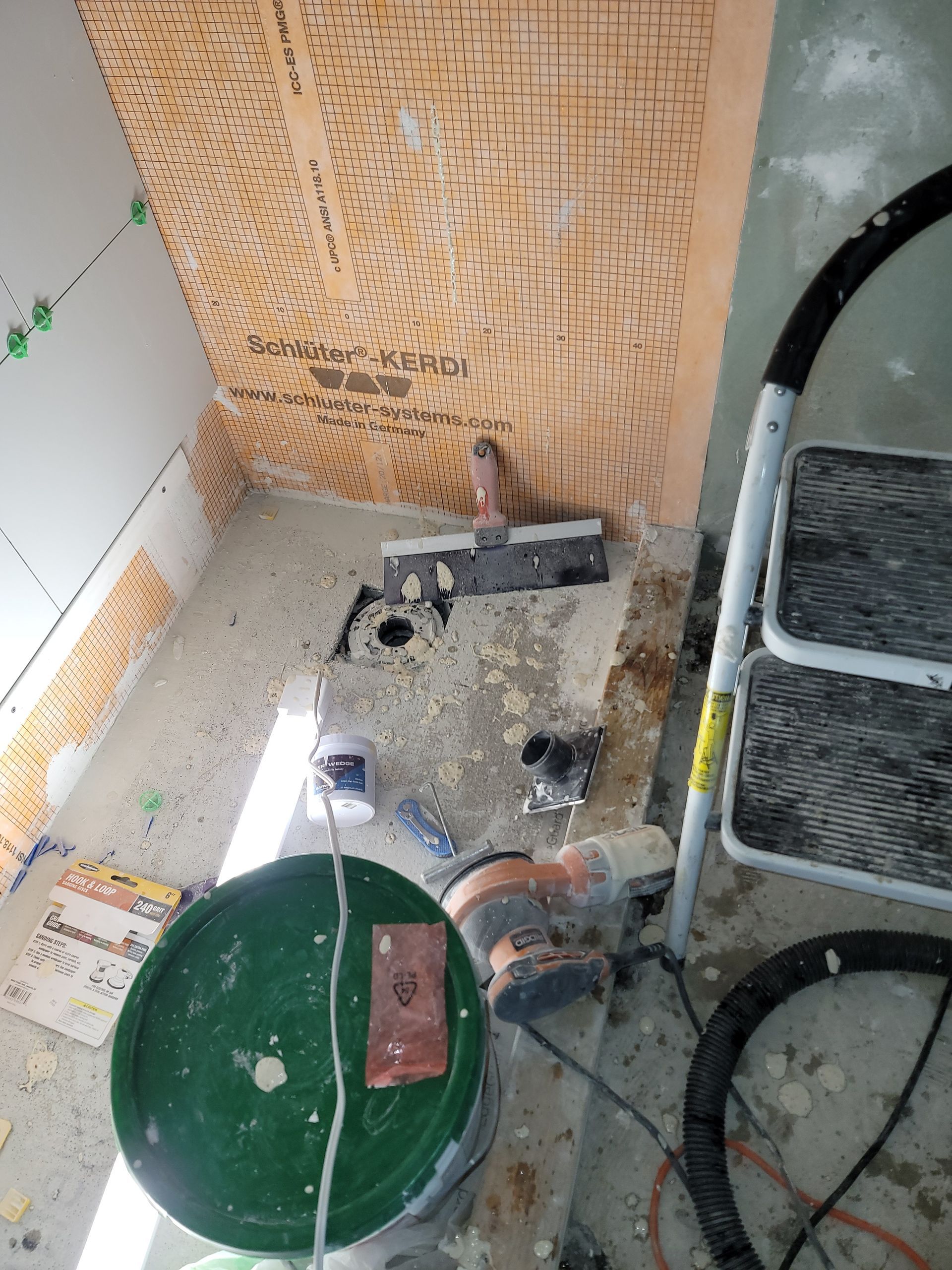 Top-down view of a cluttered work area with a green pot, tools, and a step ladder on the right.