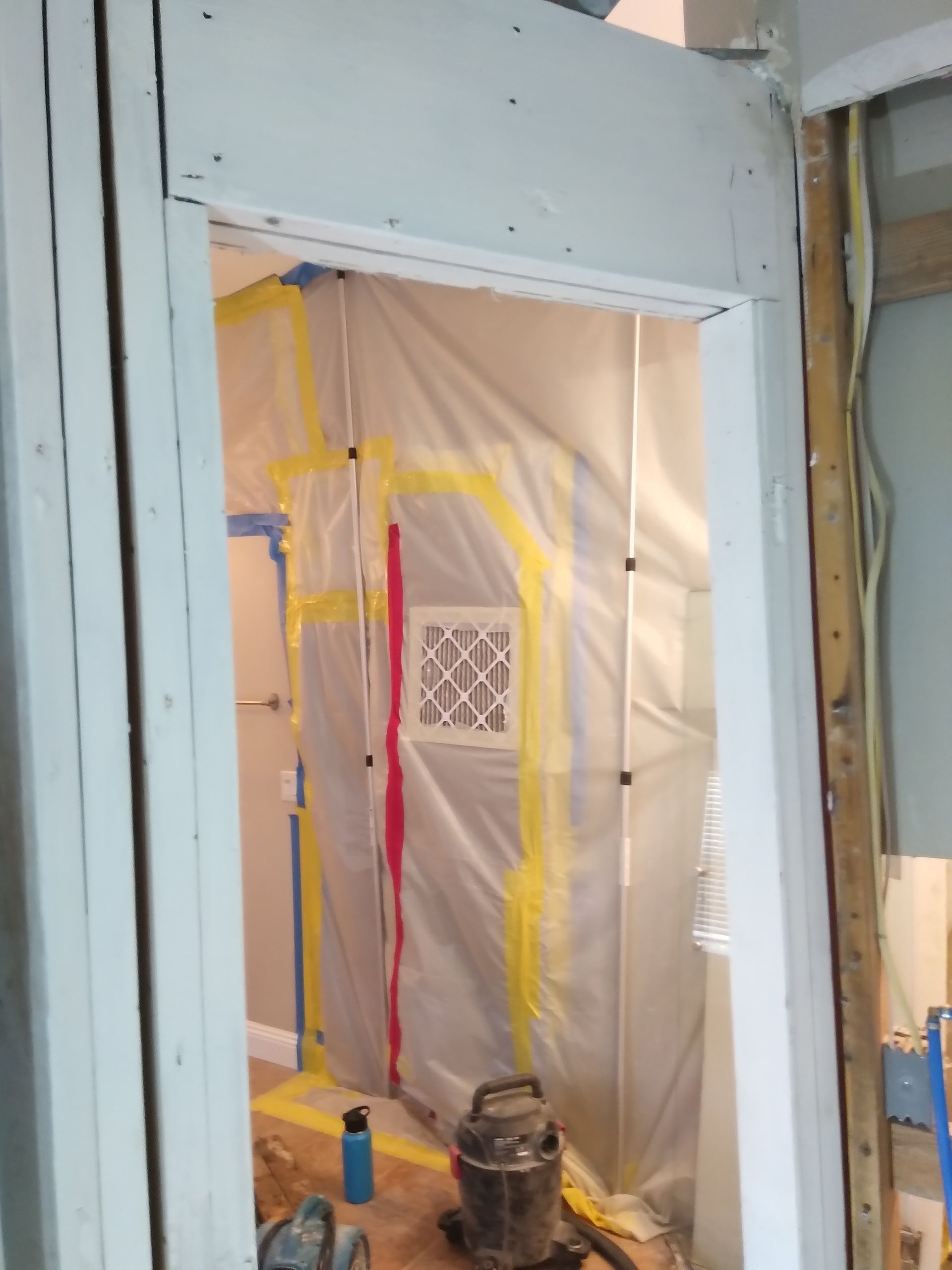 Construction area with plastic-covered doorway, taped off section, and tools on the floor.