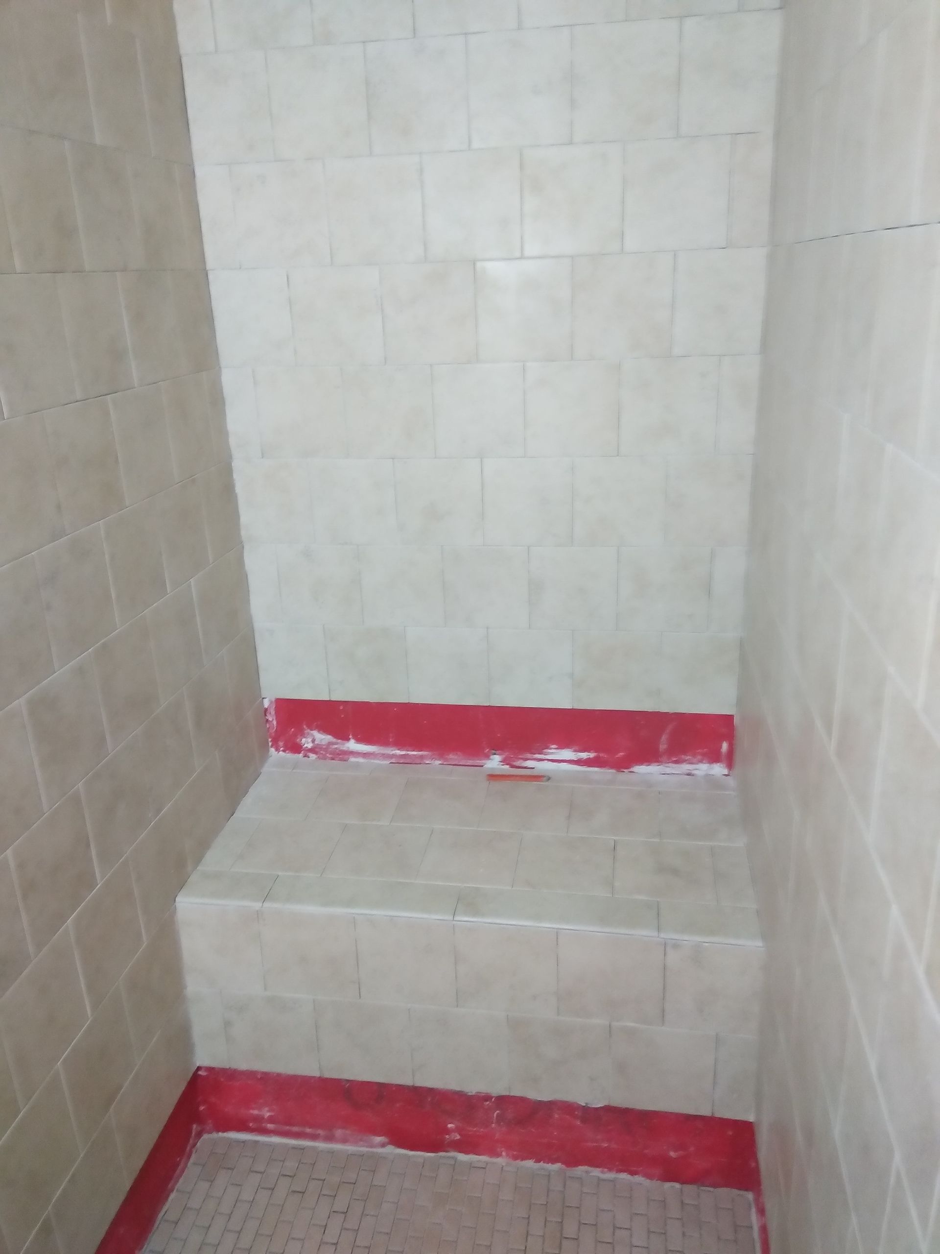 Small tiled shower corner with a raised step and red-painted edges.