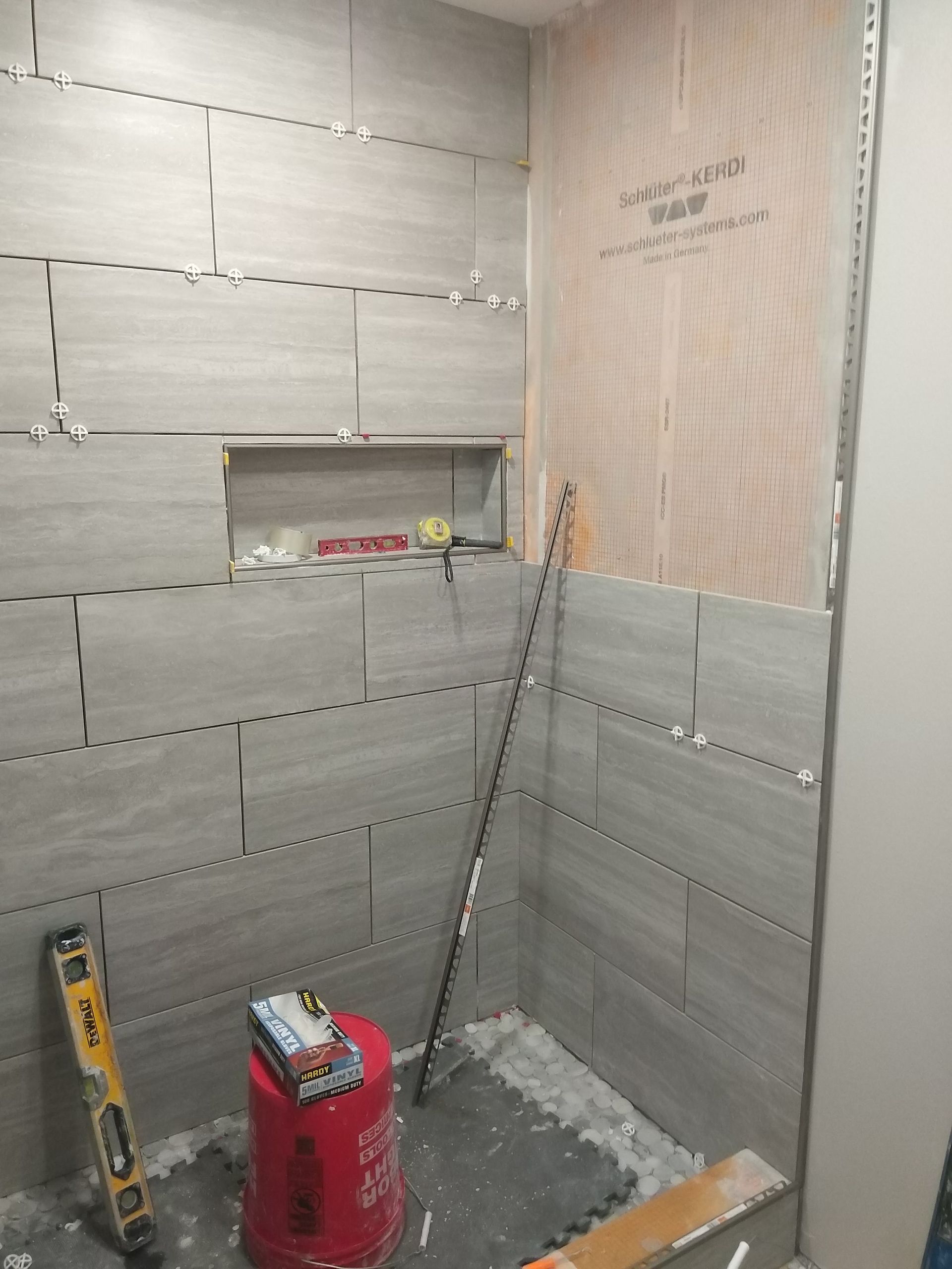 Small tiled shower under construction with a red tool, level, and leaning metal rod.