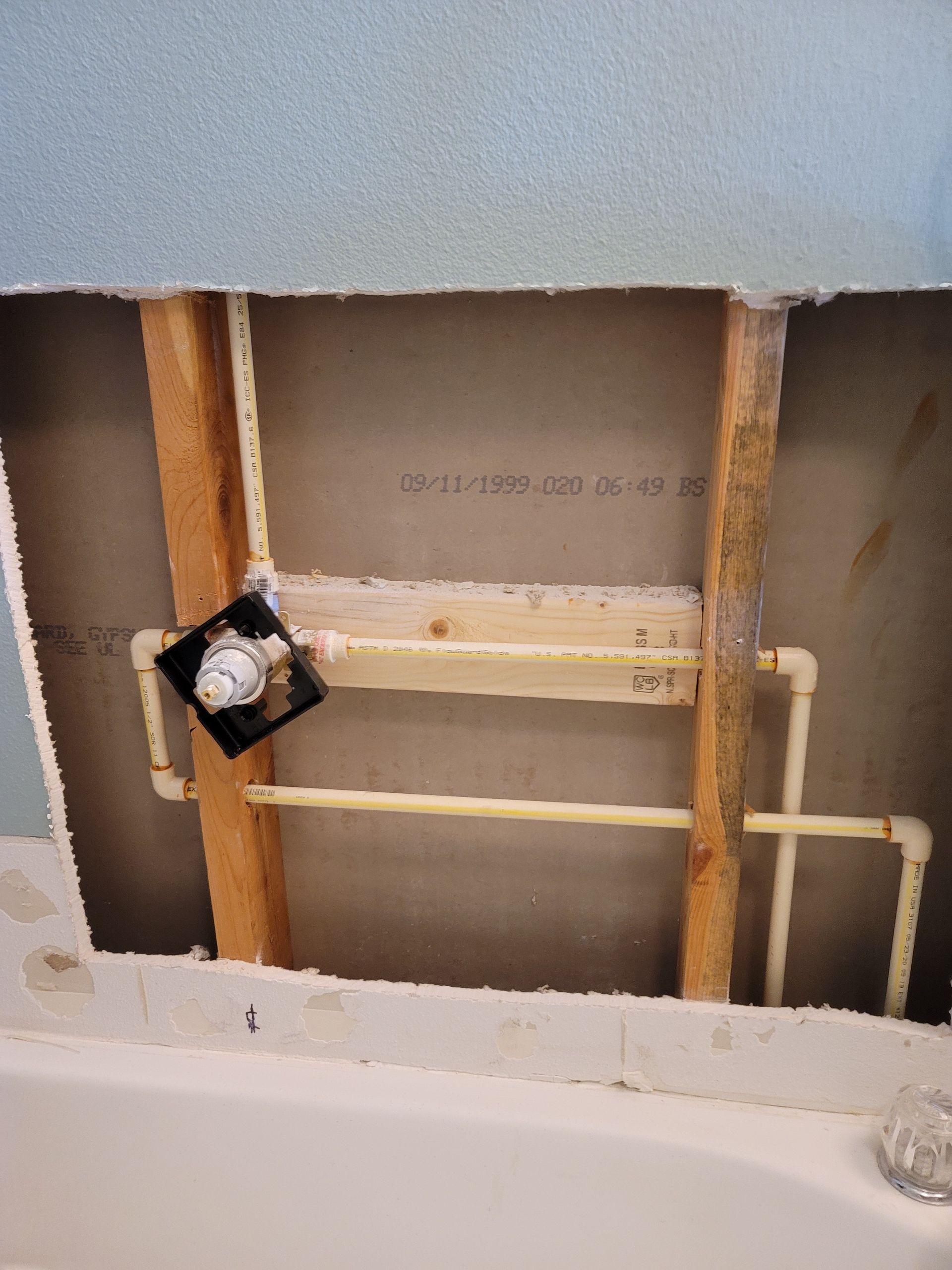 Bathroom wall opened to studs with exposed pipes and plumbing fixtures above a bathtub