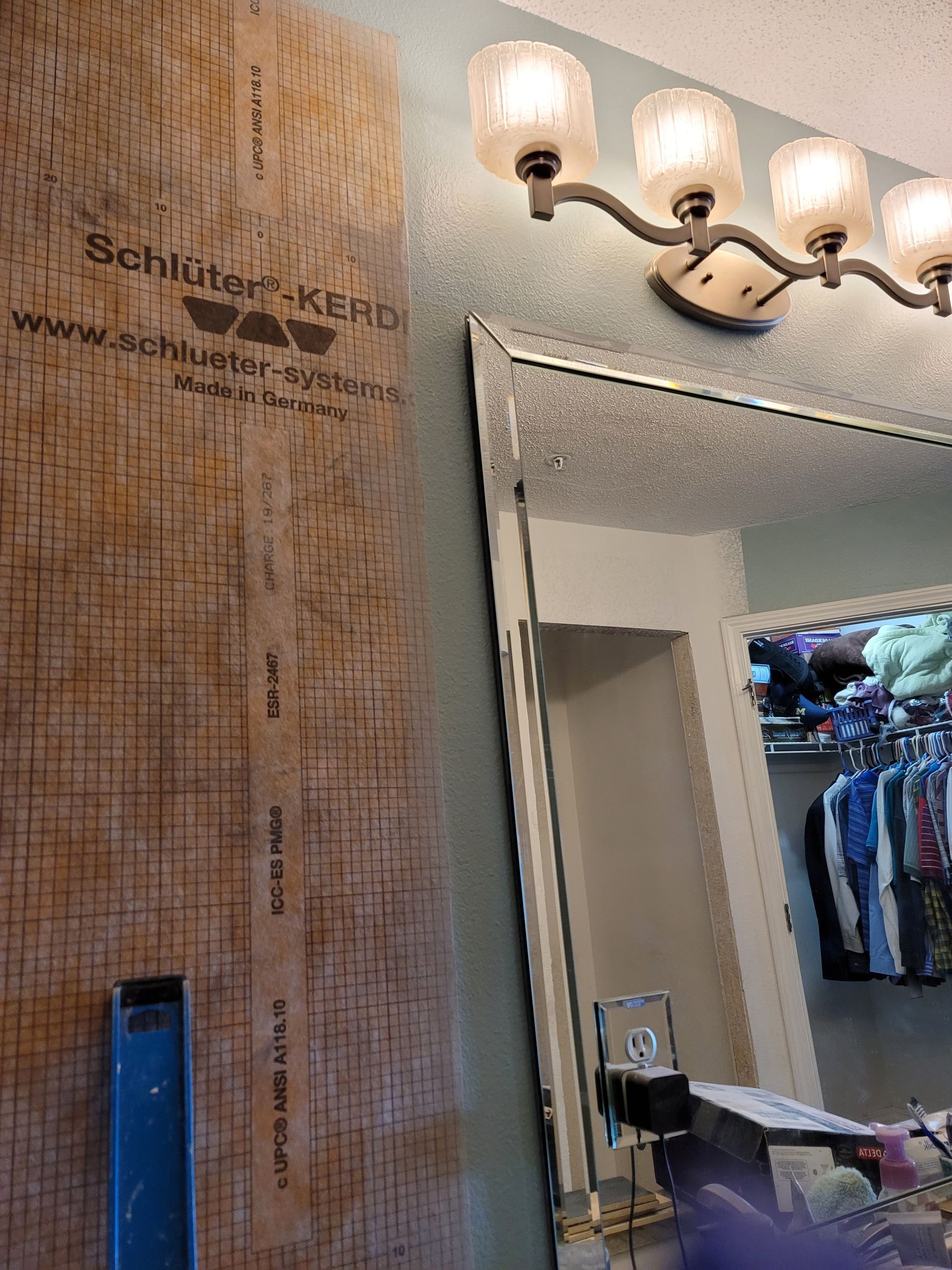 Salon mirror and vanity with lit wall sconce, wooden accent wall, and open closet in the background