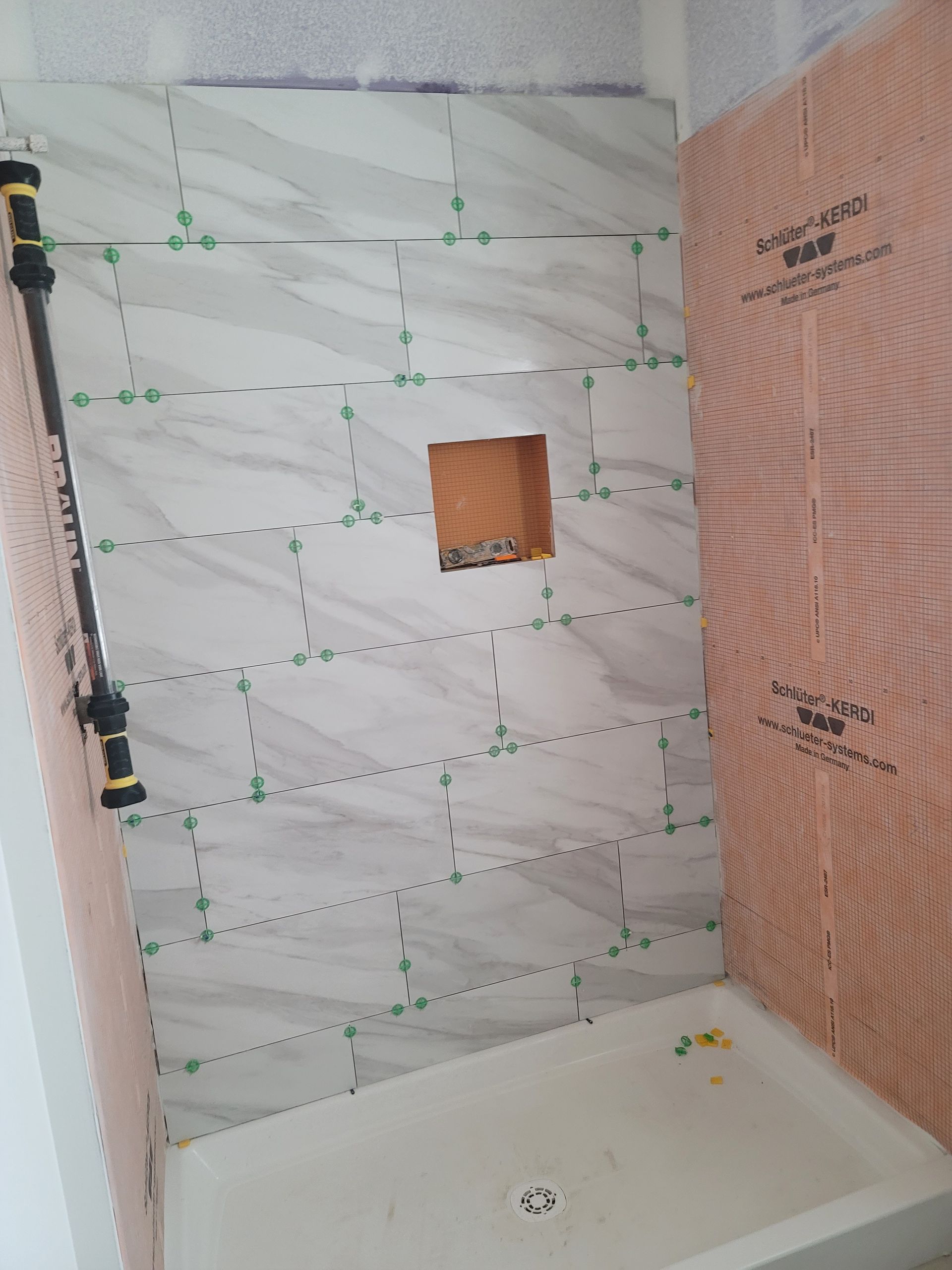 Bathroom shower under construction with white waterproof membrane and a small wall niche above the tub.