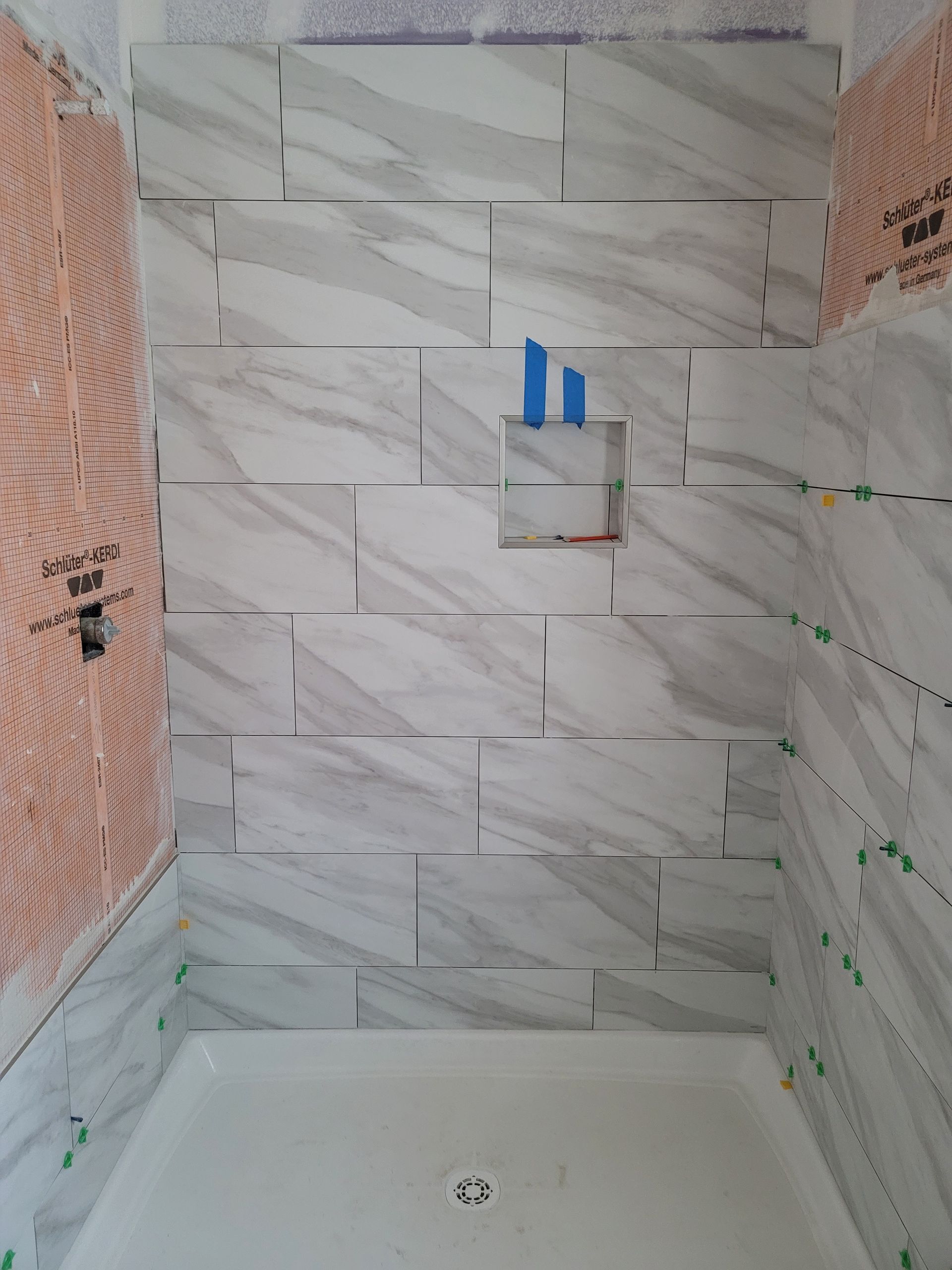 Partially tiled shower stall with white wall tiles, unfinished side walls, and plumbing fixtures visible