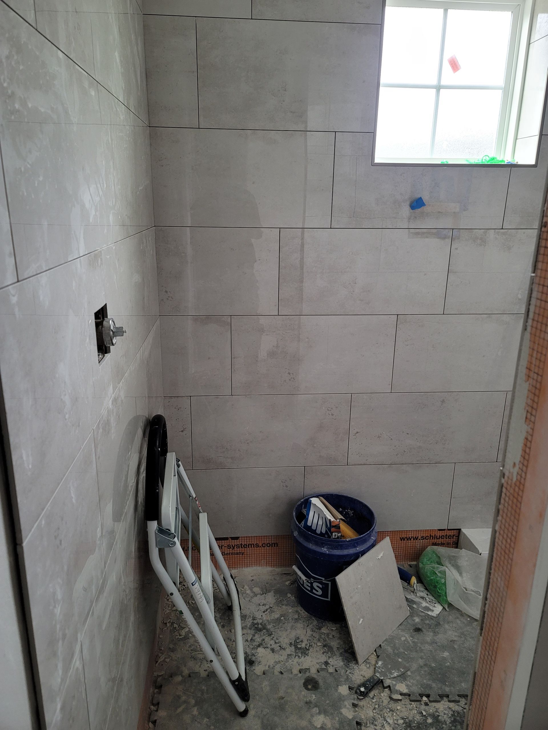 Small unfinished bathroom with gray block walls, a window, bucket, and construction debris on the floor