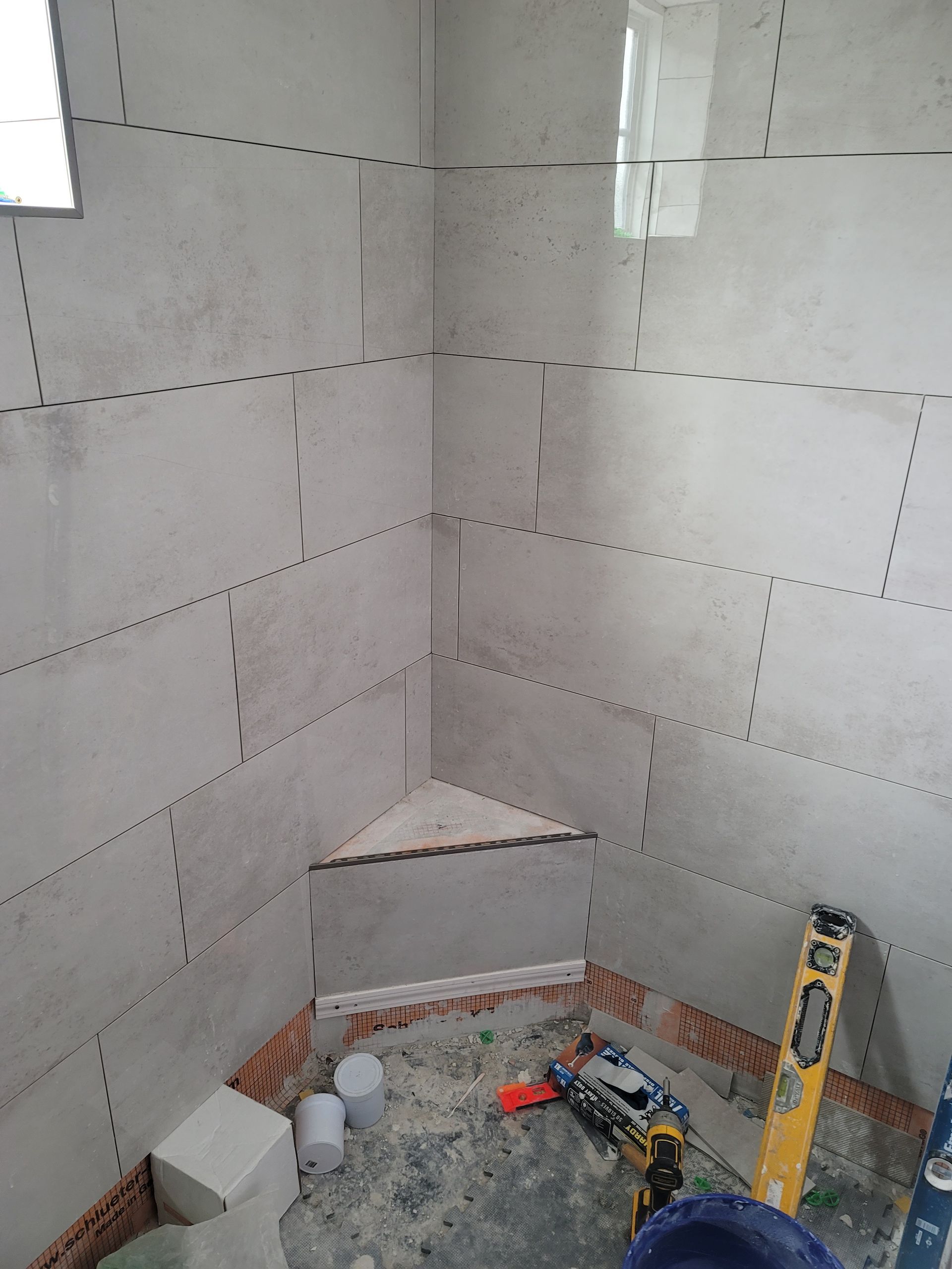 Small tiled shower corner under construction with tools and materials on the floor.