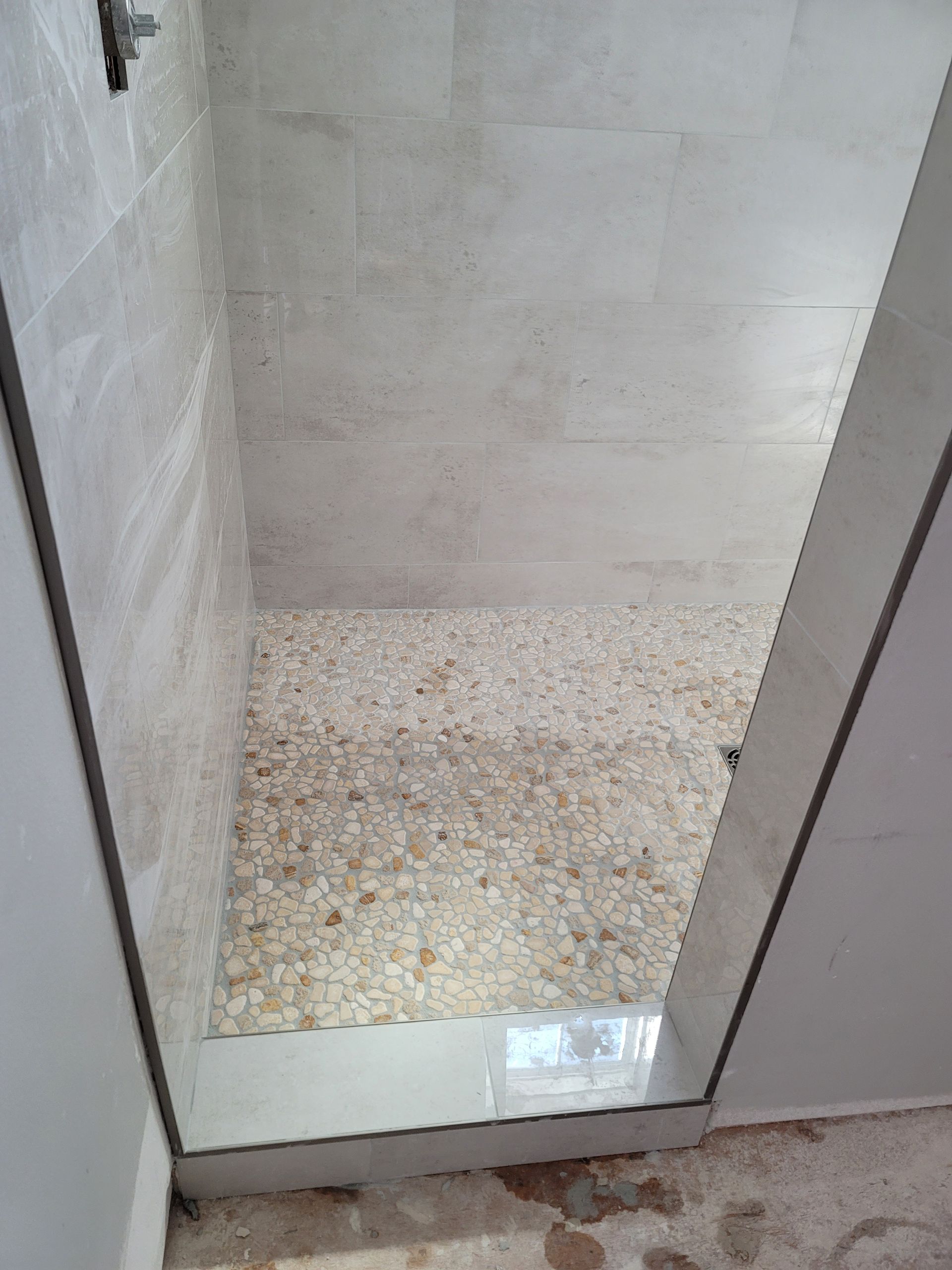 Small tiled shower stall with a textured stone floor and white walls, viewed through the doorway