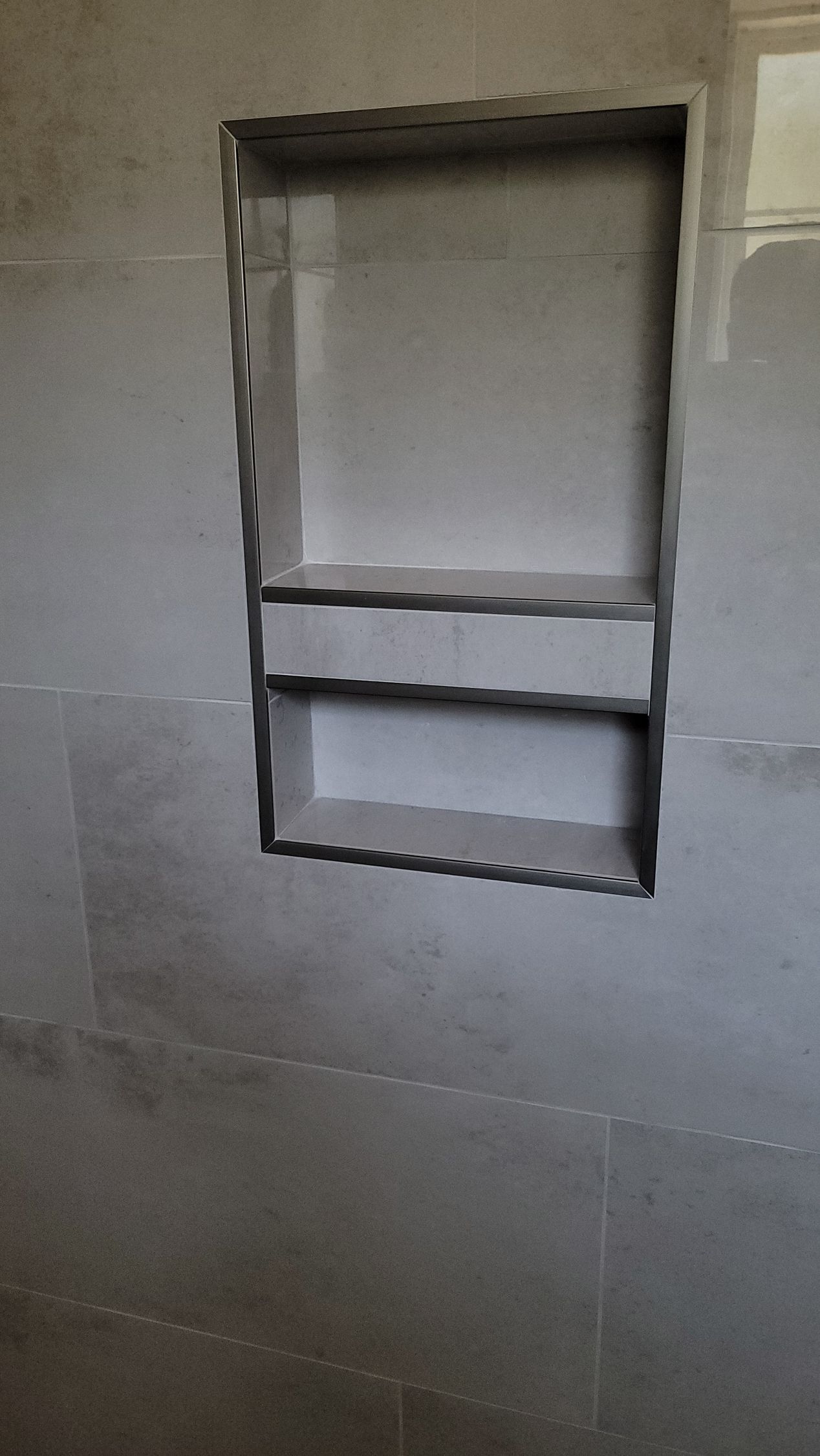 Wall niche with a metal shelf and a narrow rectangular opening in a gray tiled wall