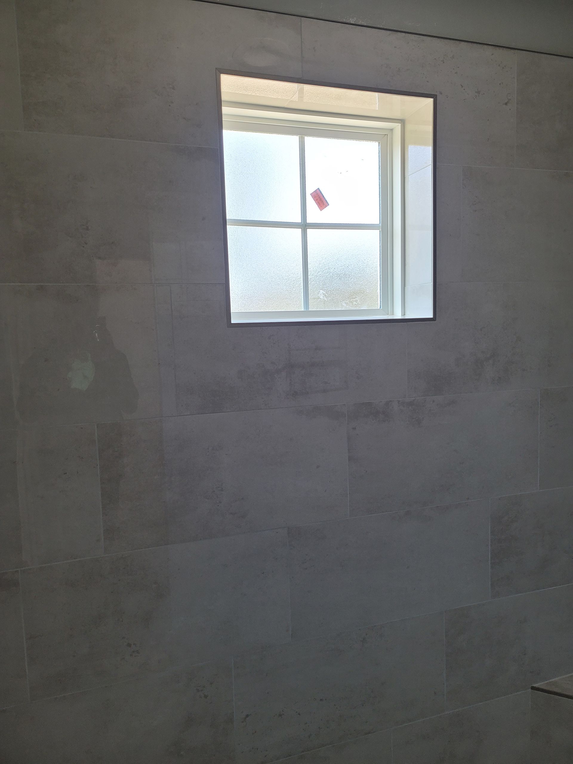 Unfinished gray wall with a small window letting in light and a bird visible outside