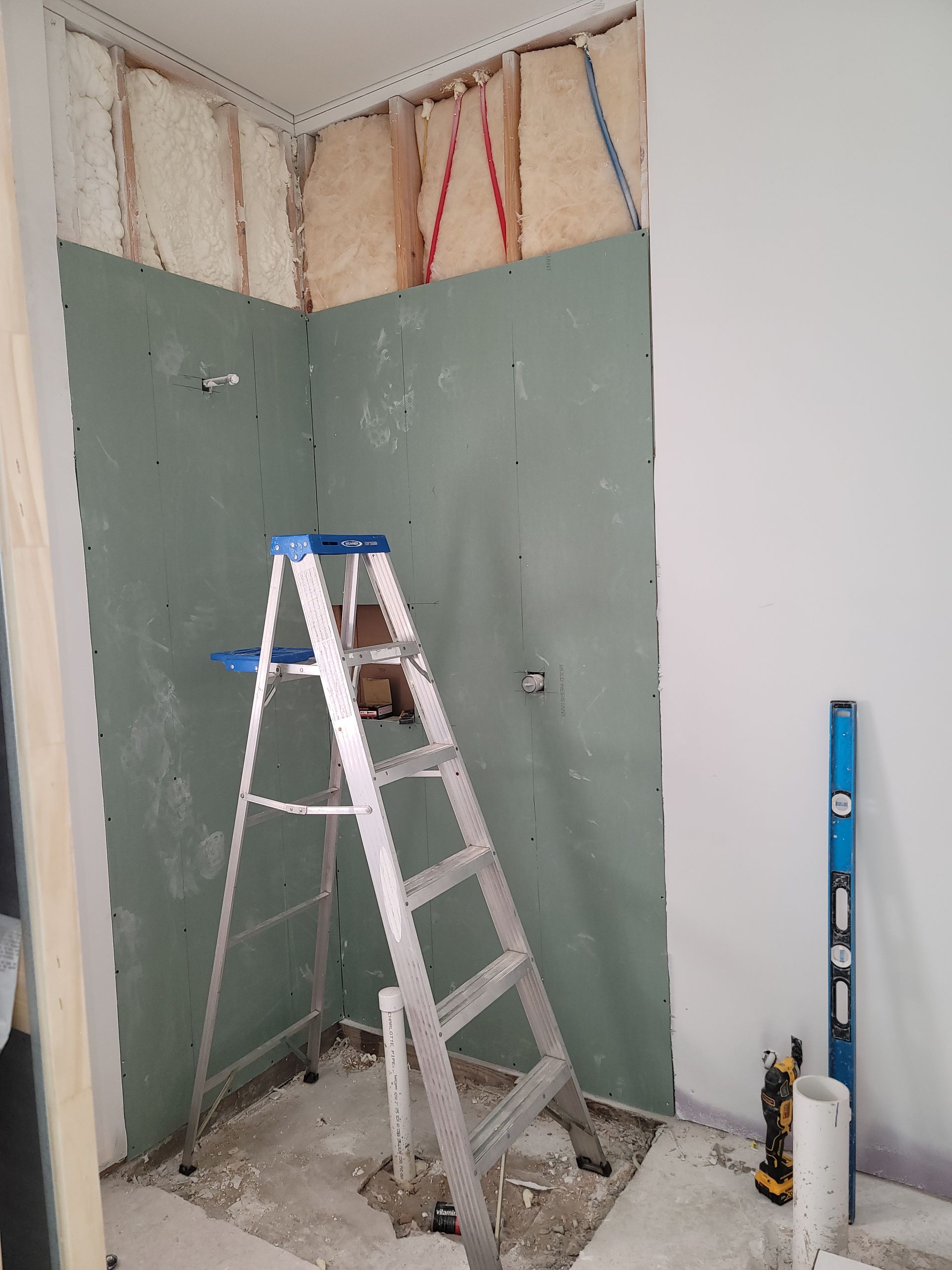 Partially renovated bathroom with green drywall, ladder, exposed insulation, and construction tools on the floor