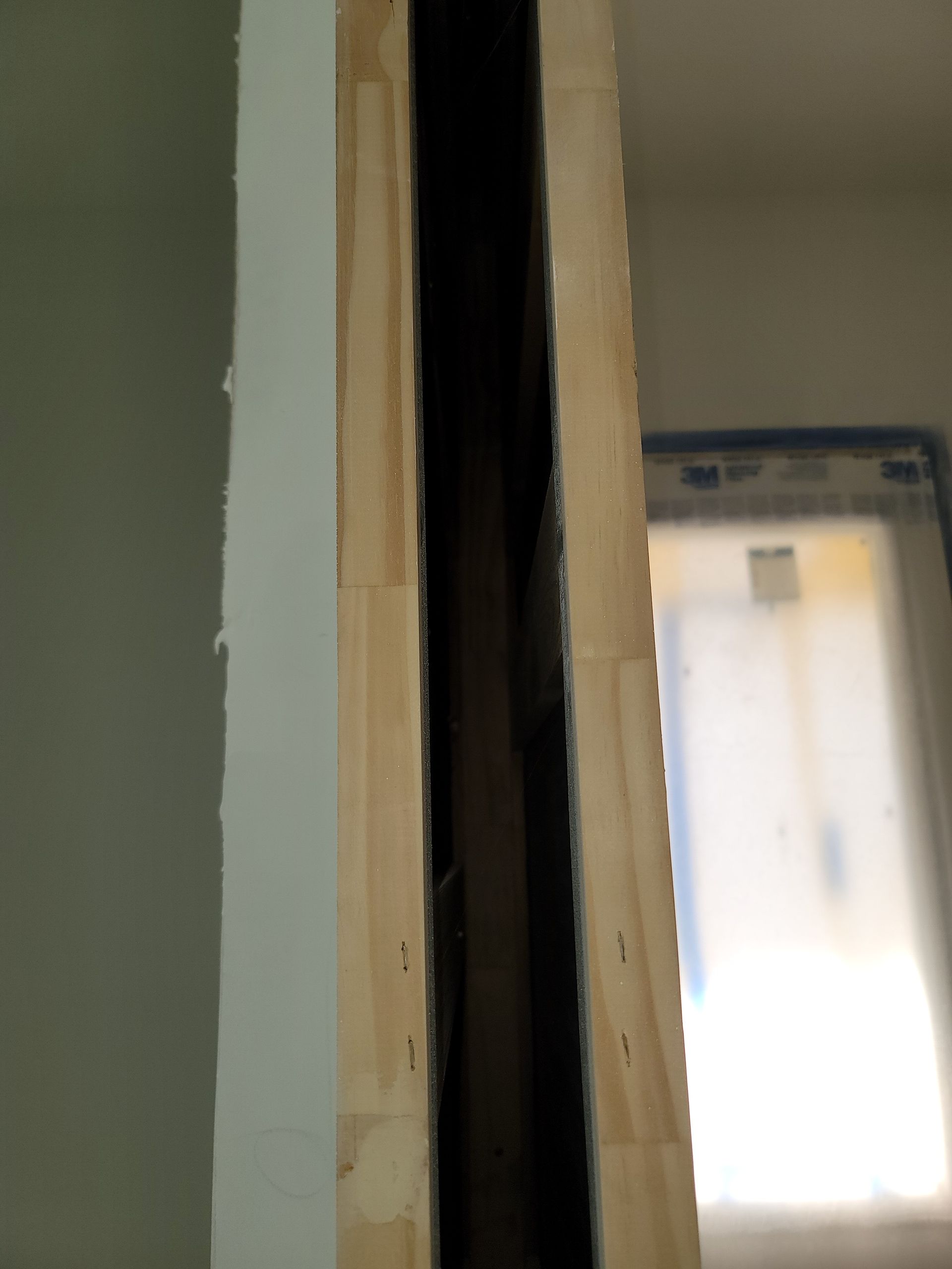 Close-up of a doorway frame with exposed wood and a bright window in the background