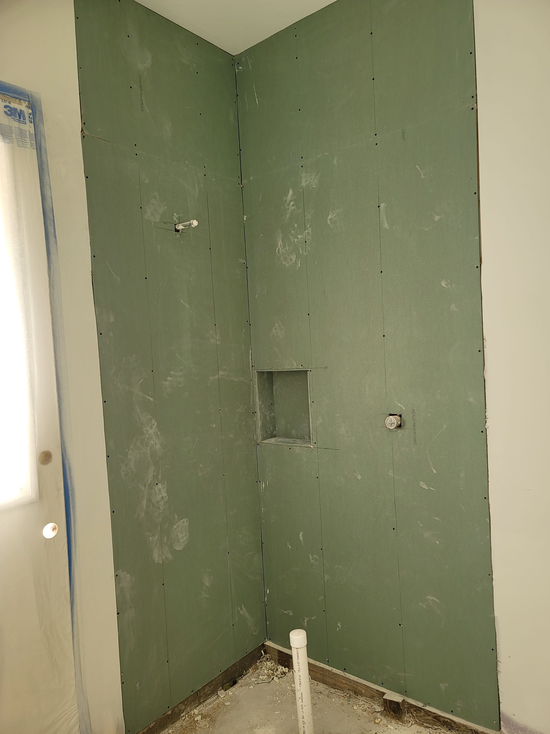 Green drywall corner with patch holes and exposed plumbing pipe in an unfinished room