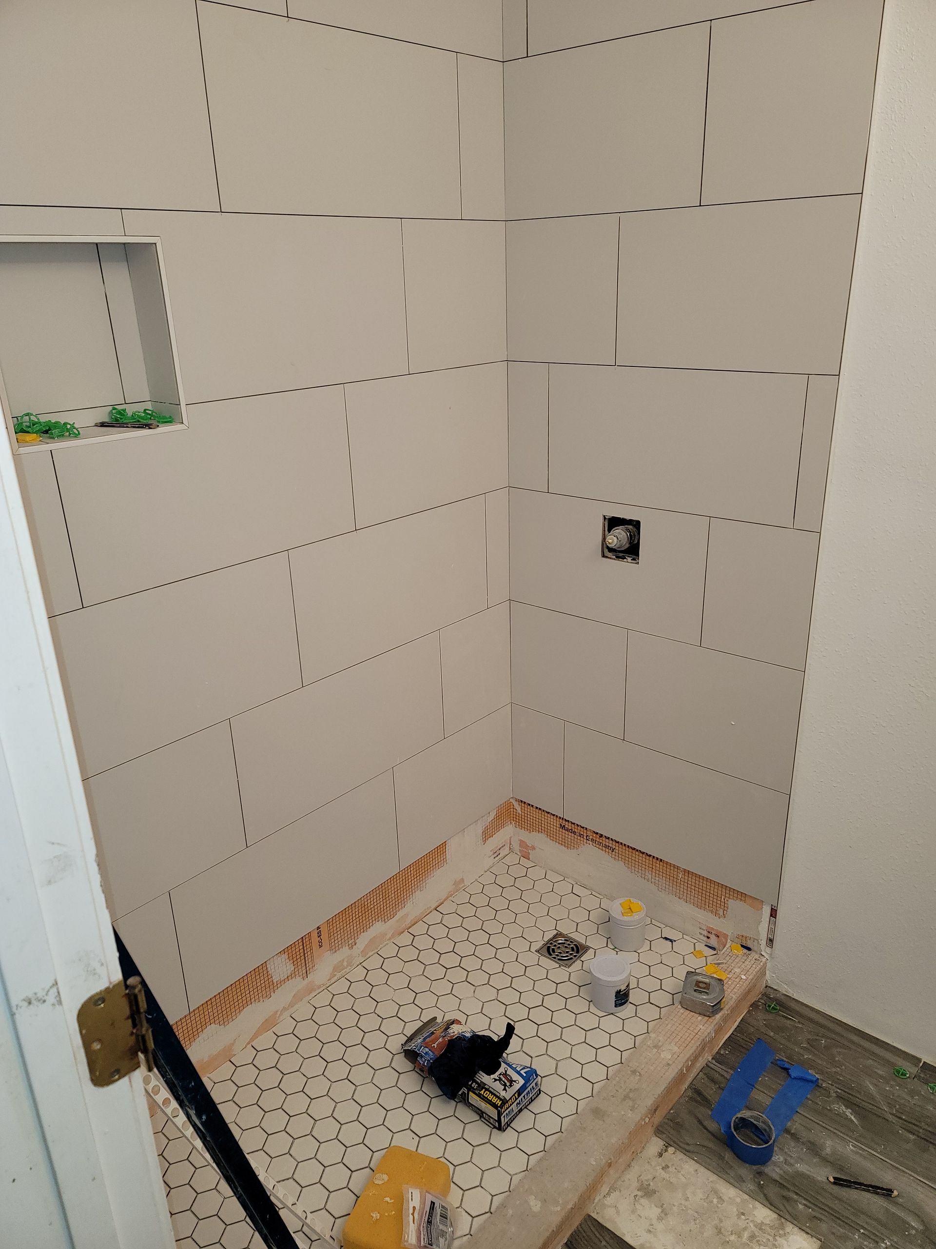 Partially tiled bathroom shower corner under renovation, with exposed wall panels and tools on the floor