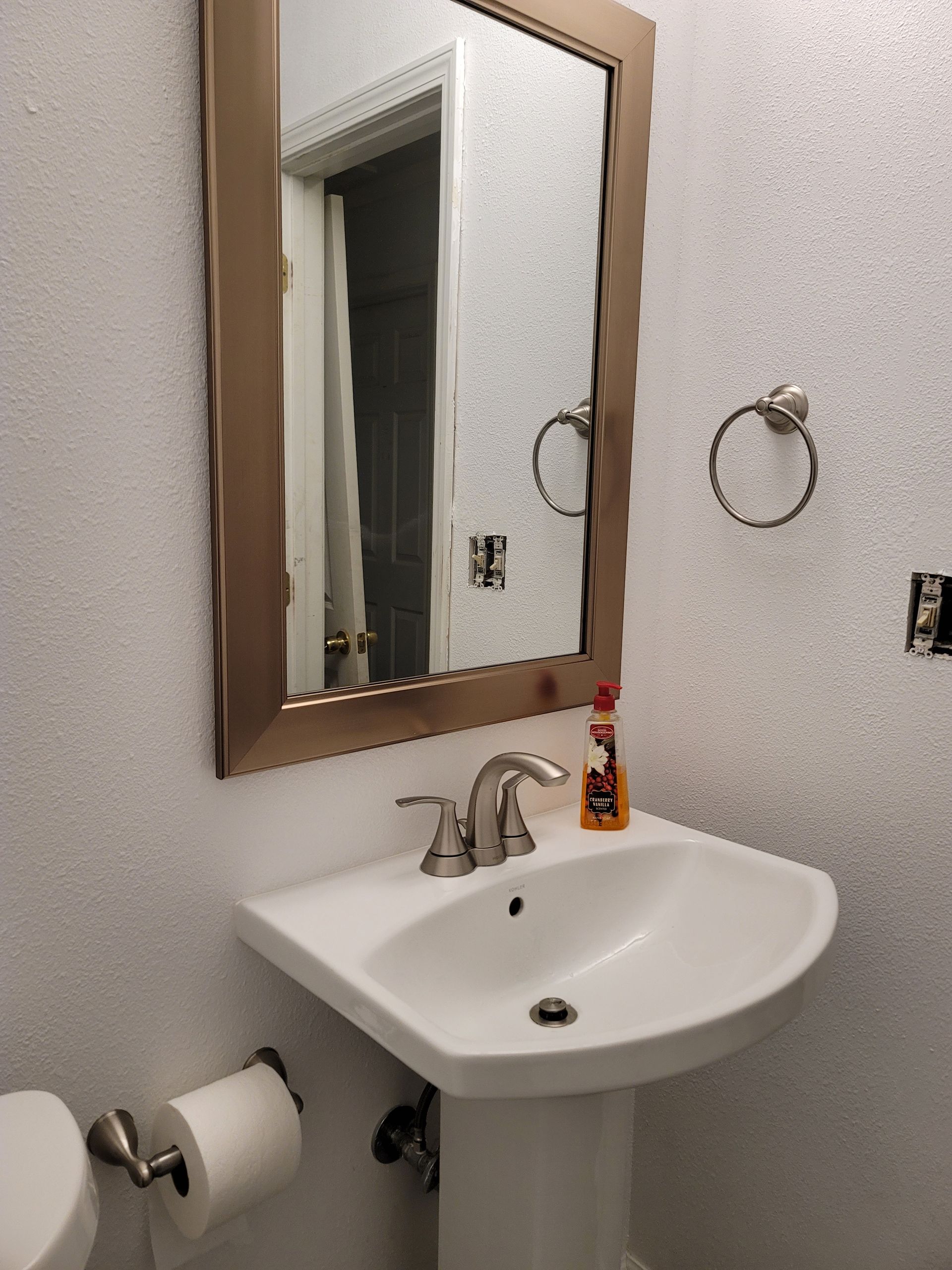Small bathroom with wall mirror, white sink, towel ring, and toilet paper holder.