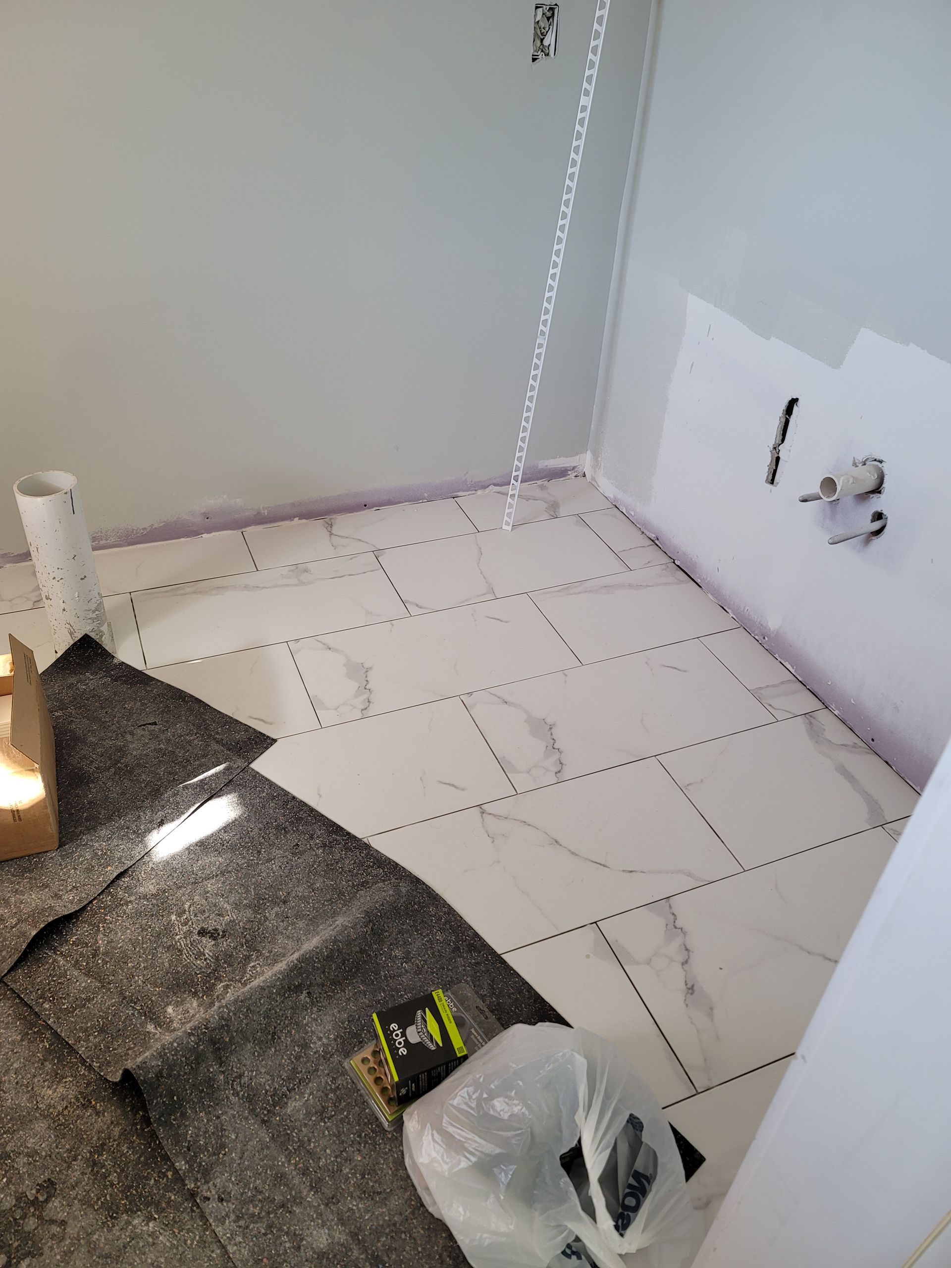 Small bathroom under renovation with tiled floor, exposed wall plumbing, and tools on the floor.