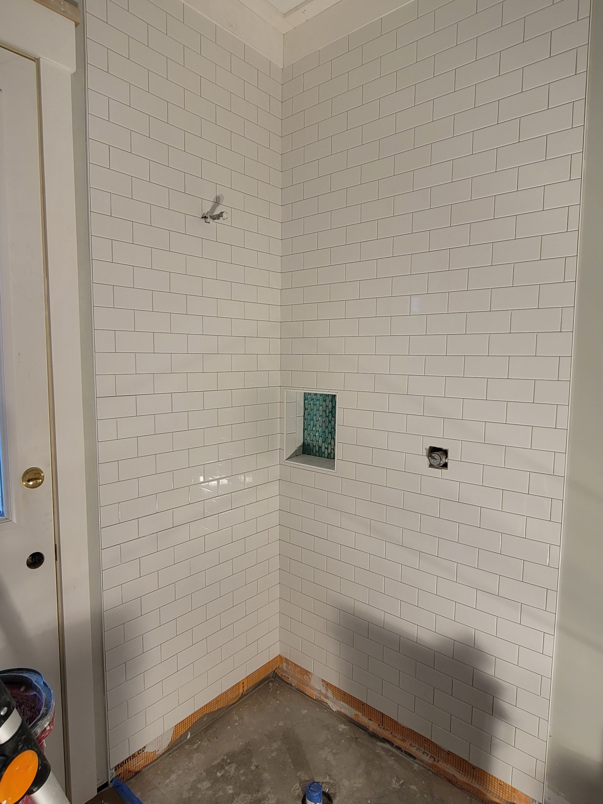 Empty white-tiled corner with a small wall opening, outlets, and concrete floor in a room under construction