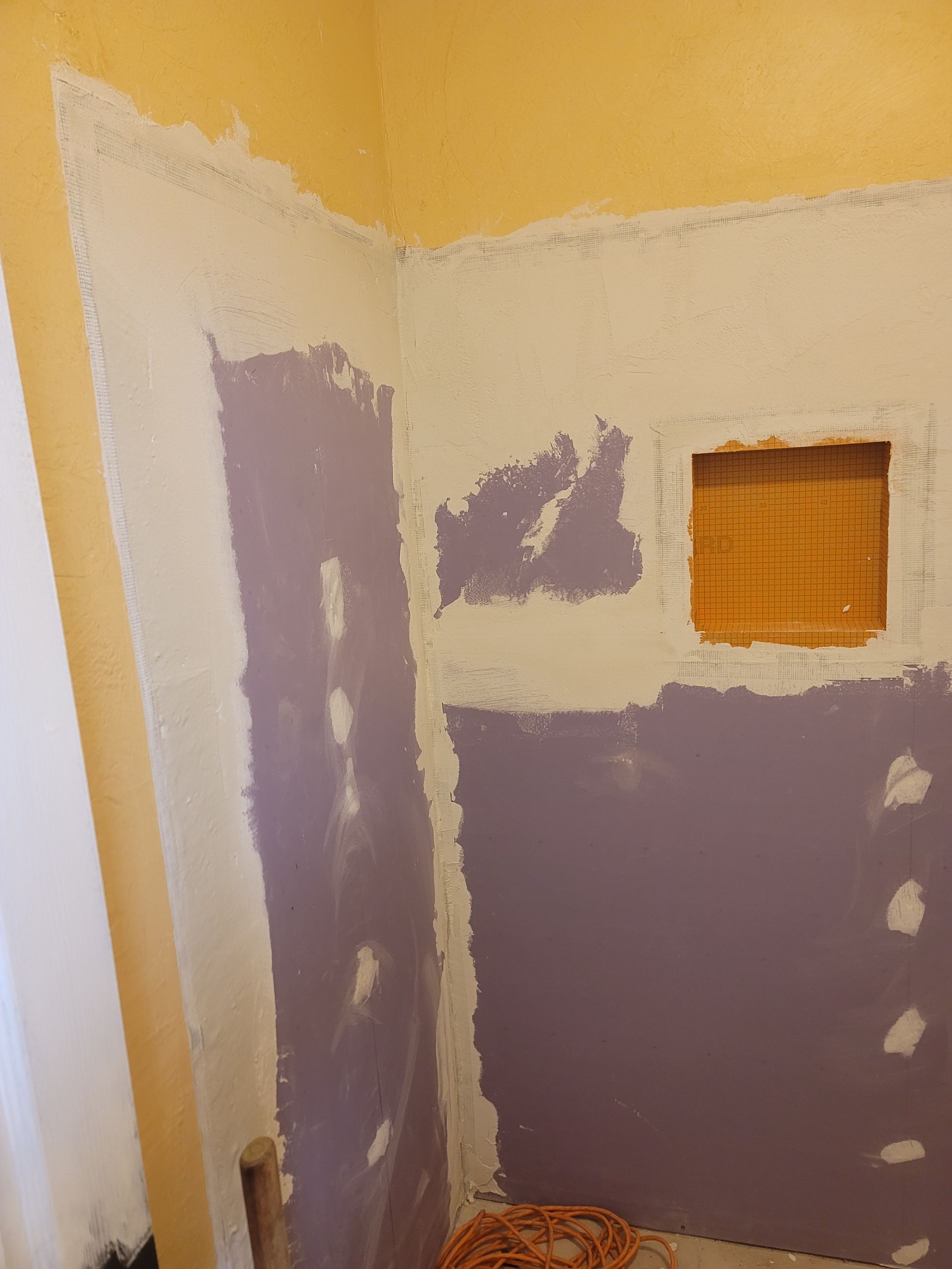 Partially painted bathroom wall with purple primer and a small square vent opening