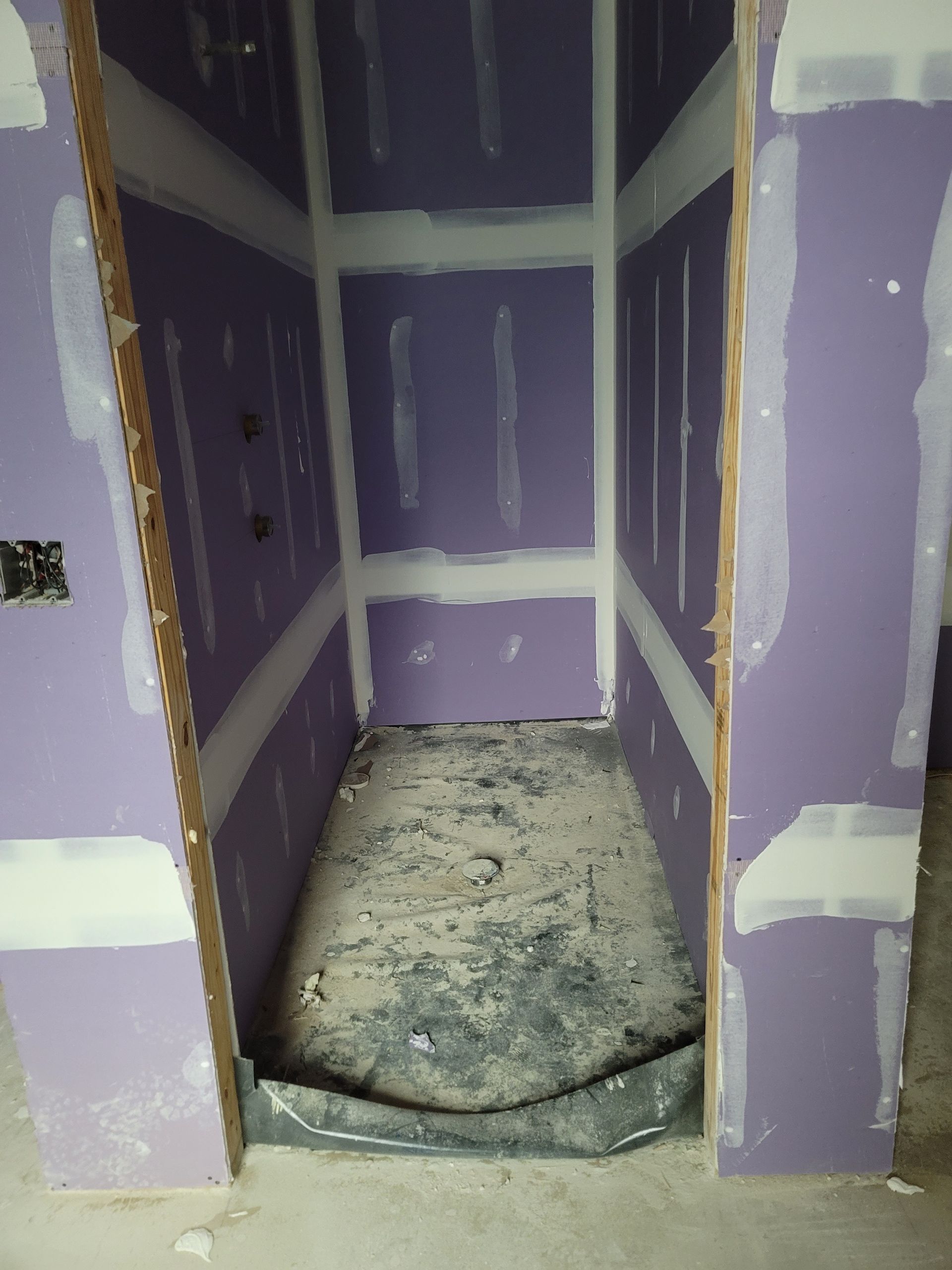 Small unfinished drywall closet with purple walls and a dusty concrete floor.