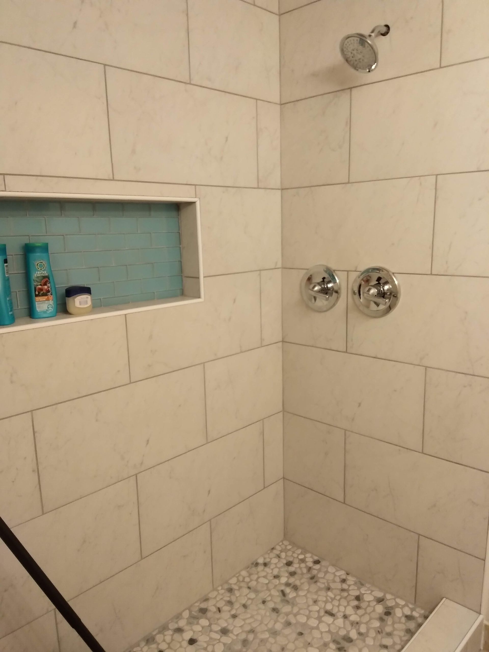 Tiled shower with built-in niche holding toiletries, chrome controls, and pebble floor.