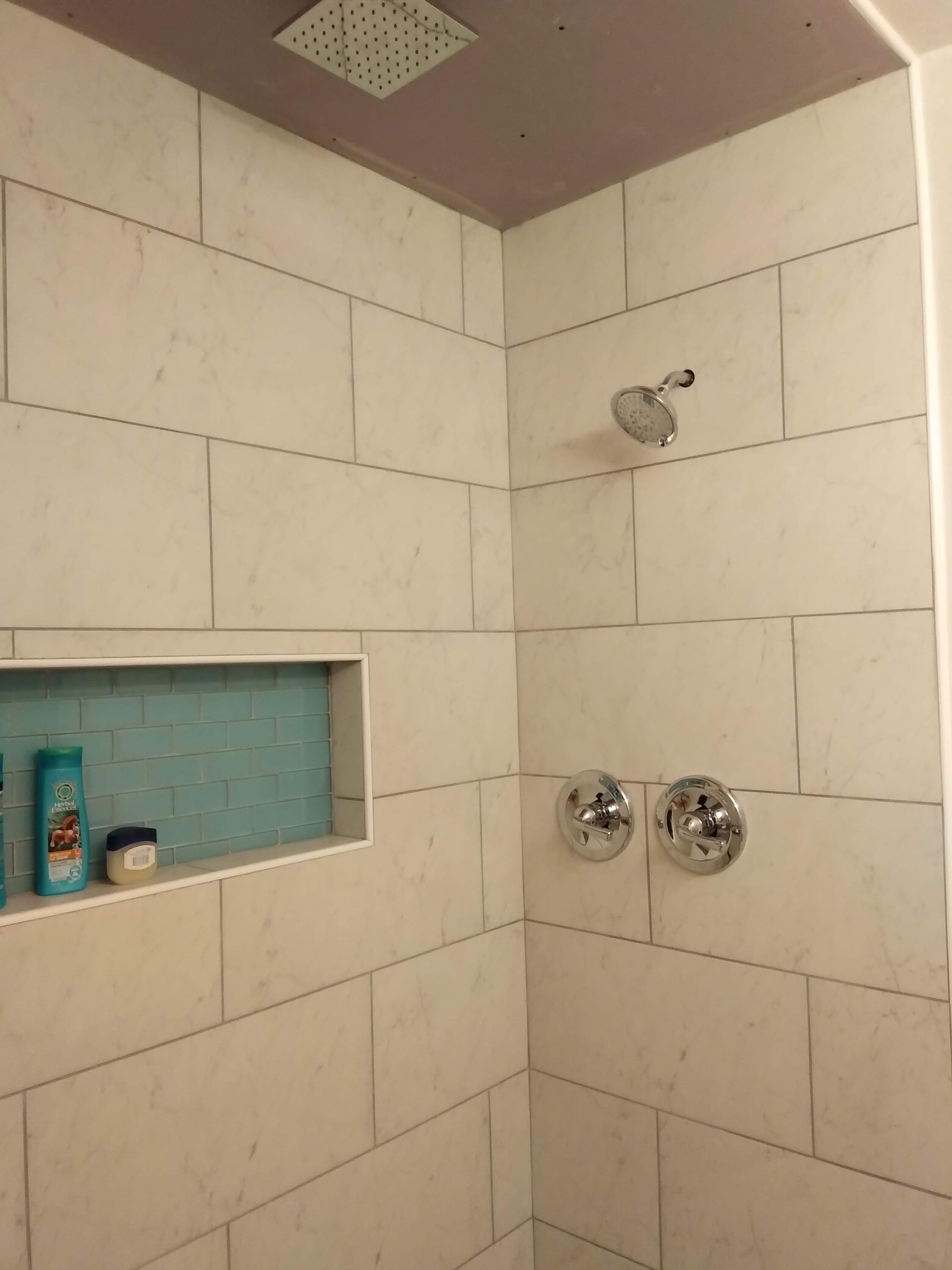 Empty tiled shower with a recessed shelf, chrome shower controls, and a showerhead.