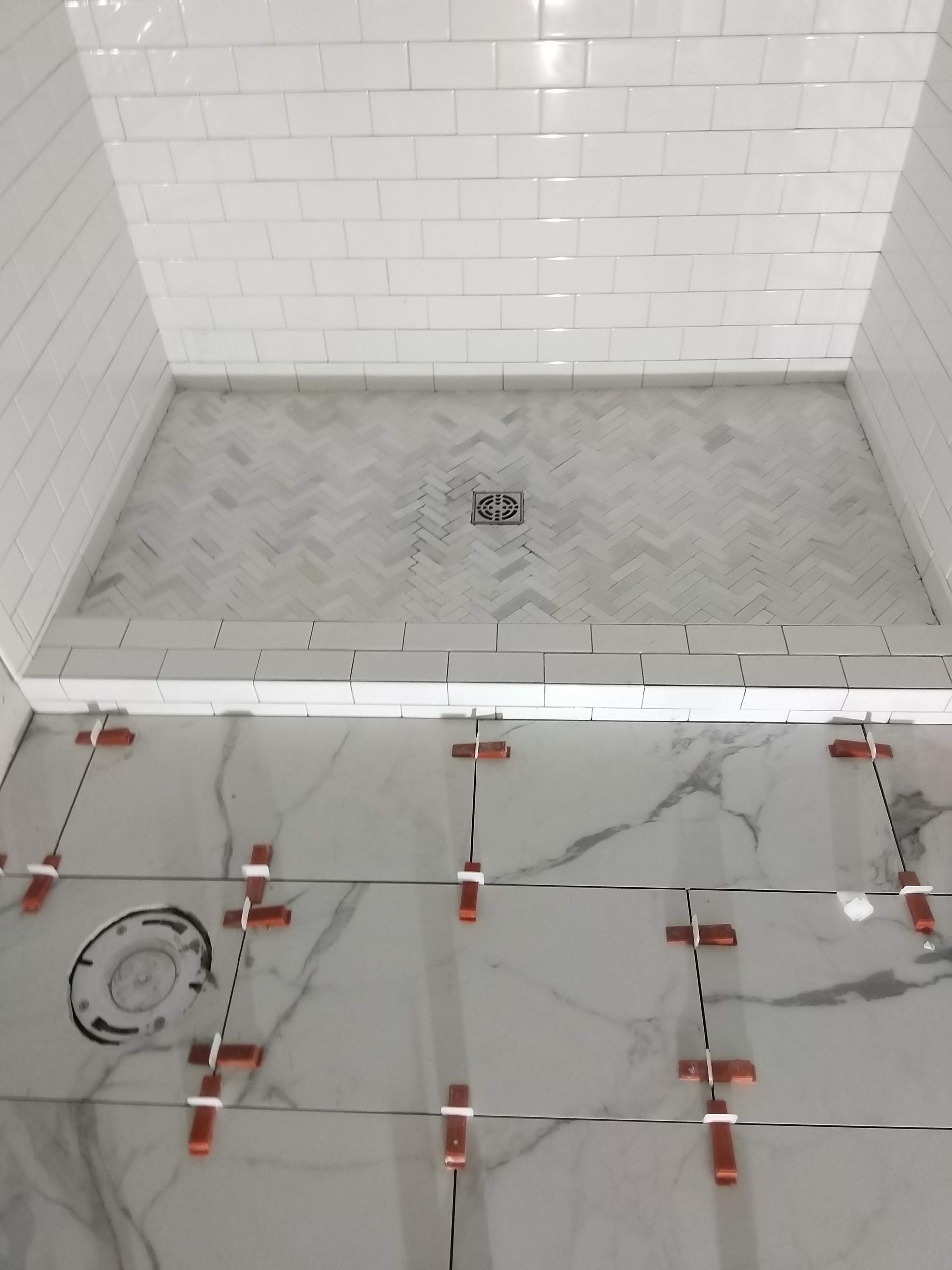 White-tiled shower floor under construction with red tile spacers and a drain hole.
