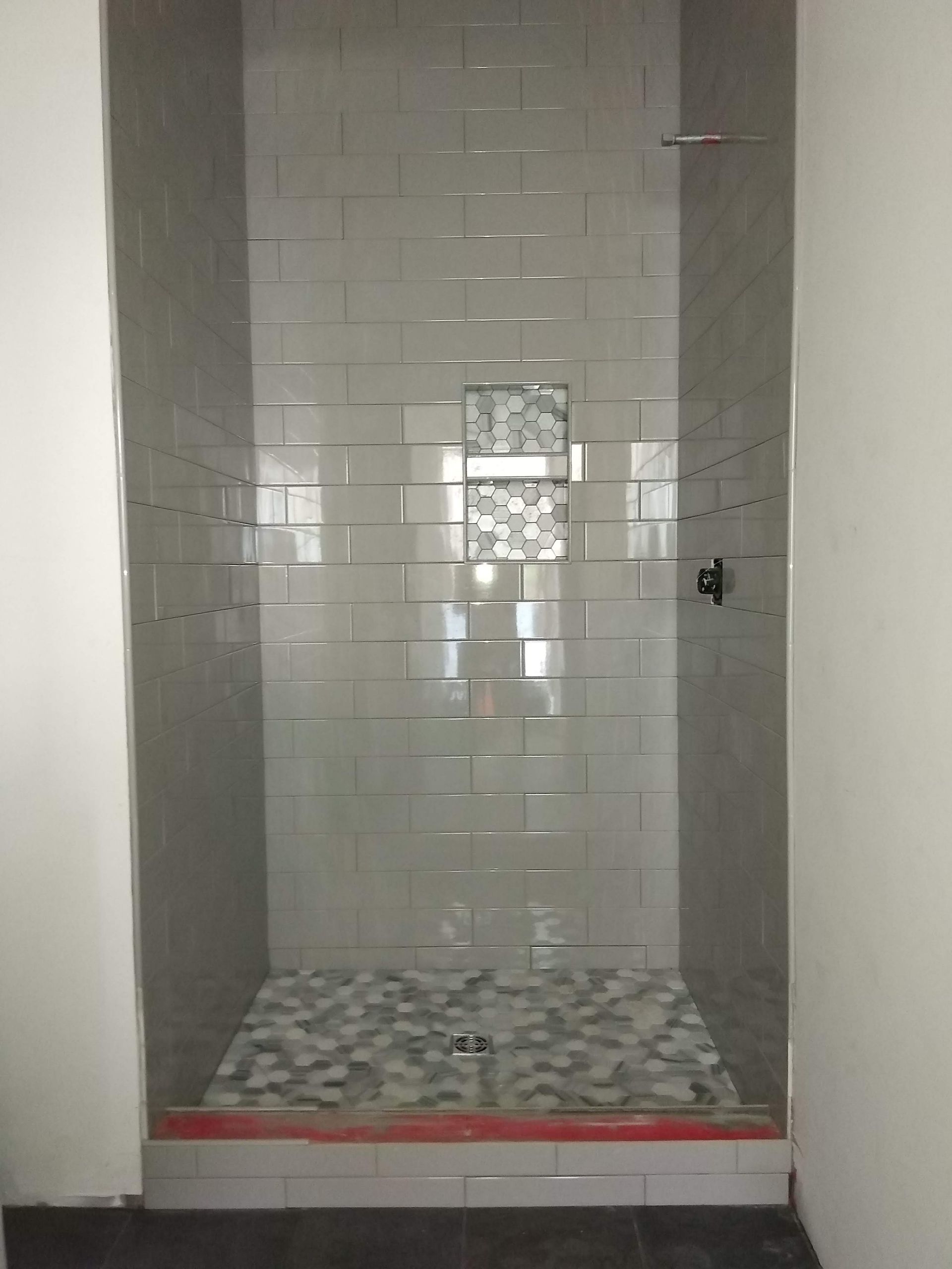 Empty tiled shower stall with mosaic floor, grab bar, and recessed soap niche.