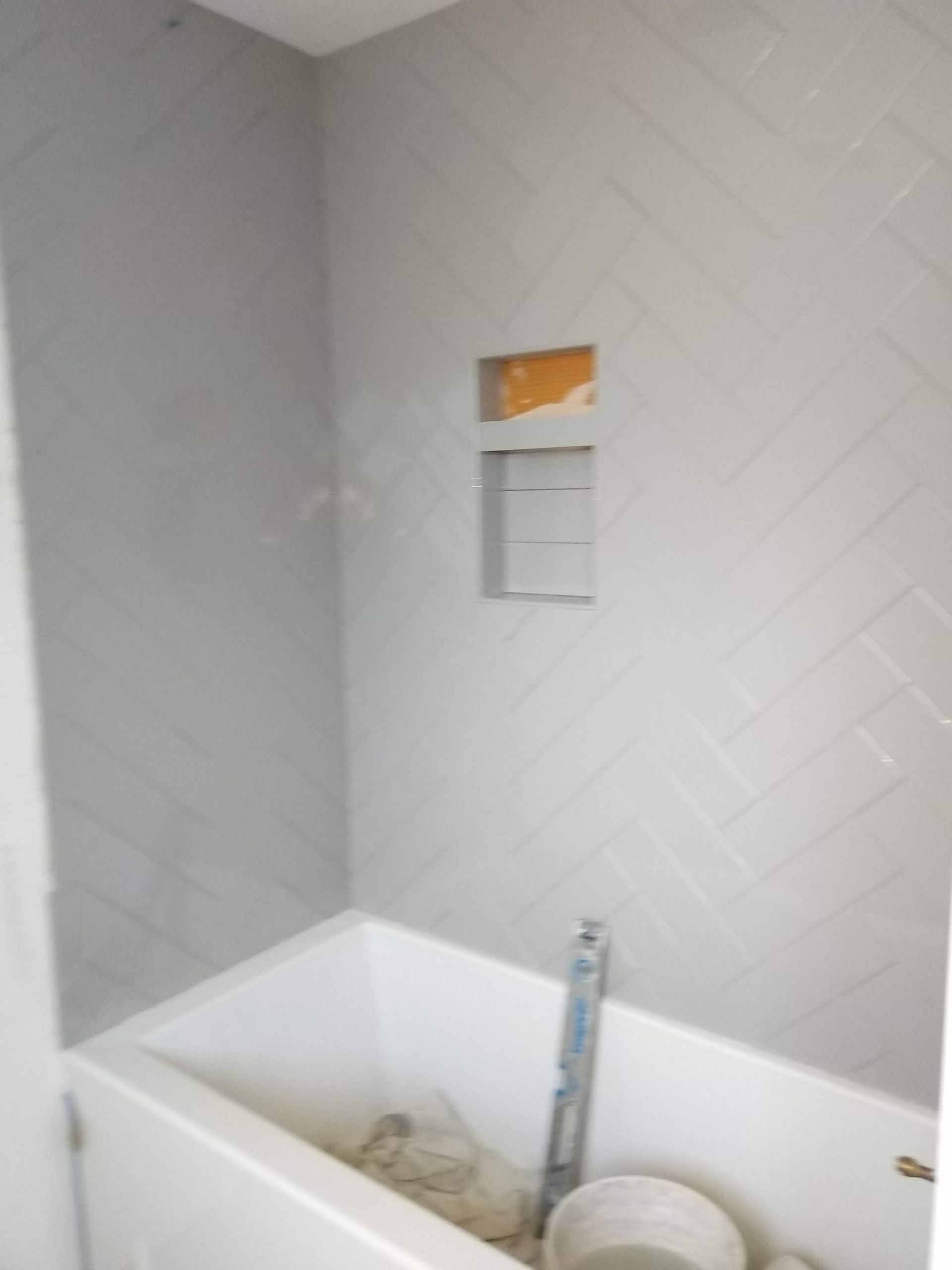 Bathroom shower with white tile walls and a partially installed bathtub faucet